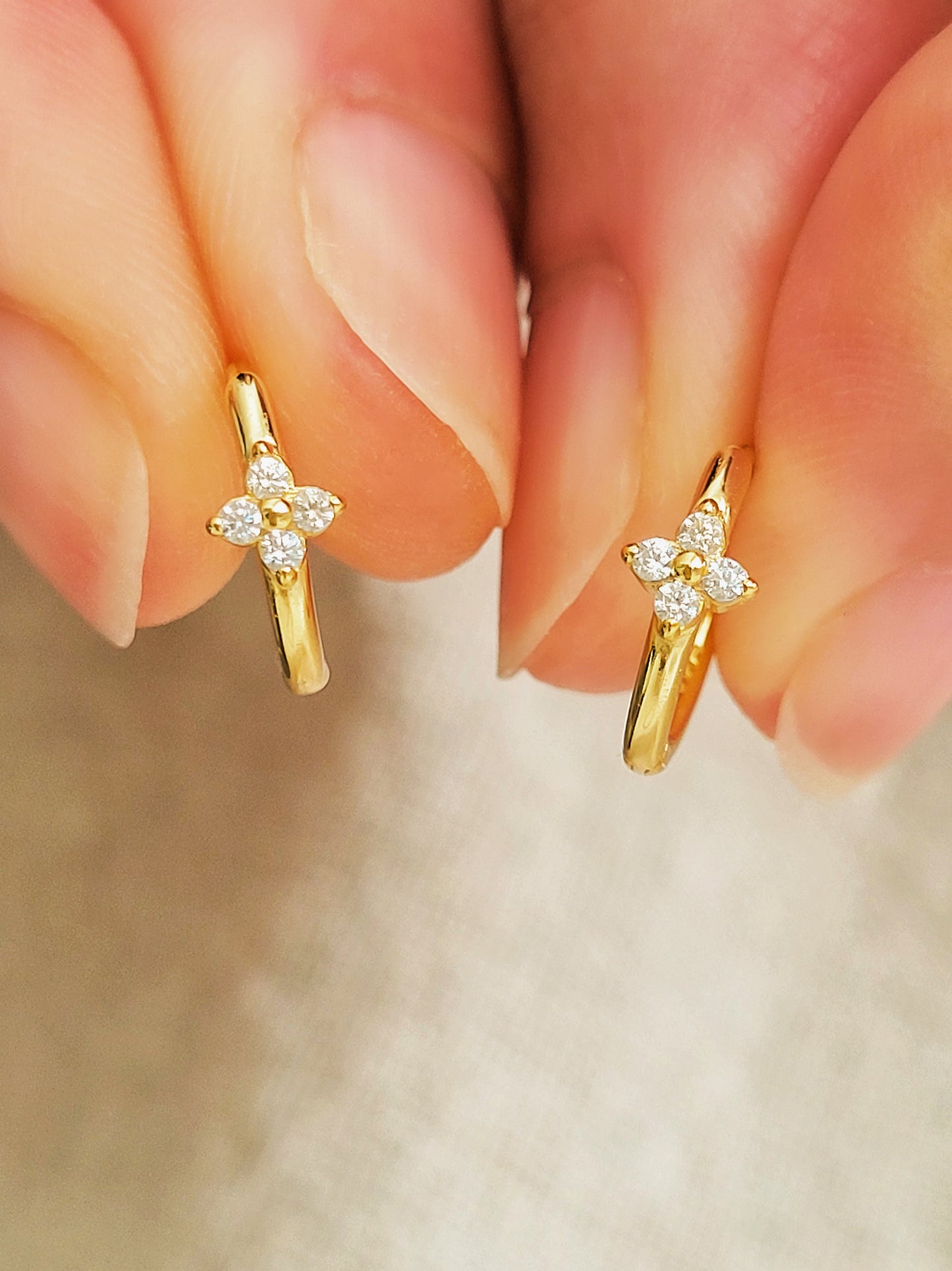 Close up of a pair of gold clover huggie hoop earrings, small gold hoop design with zirconia accents.