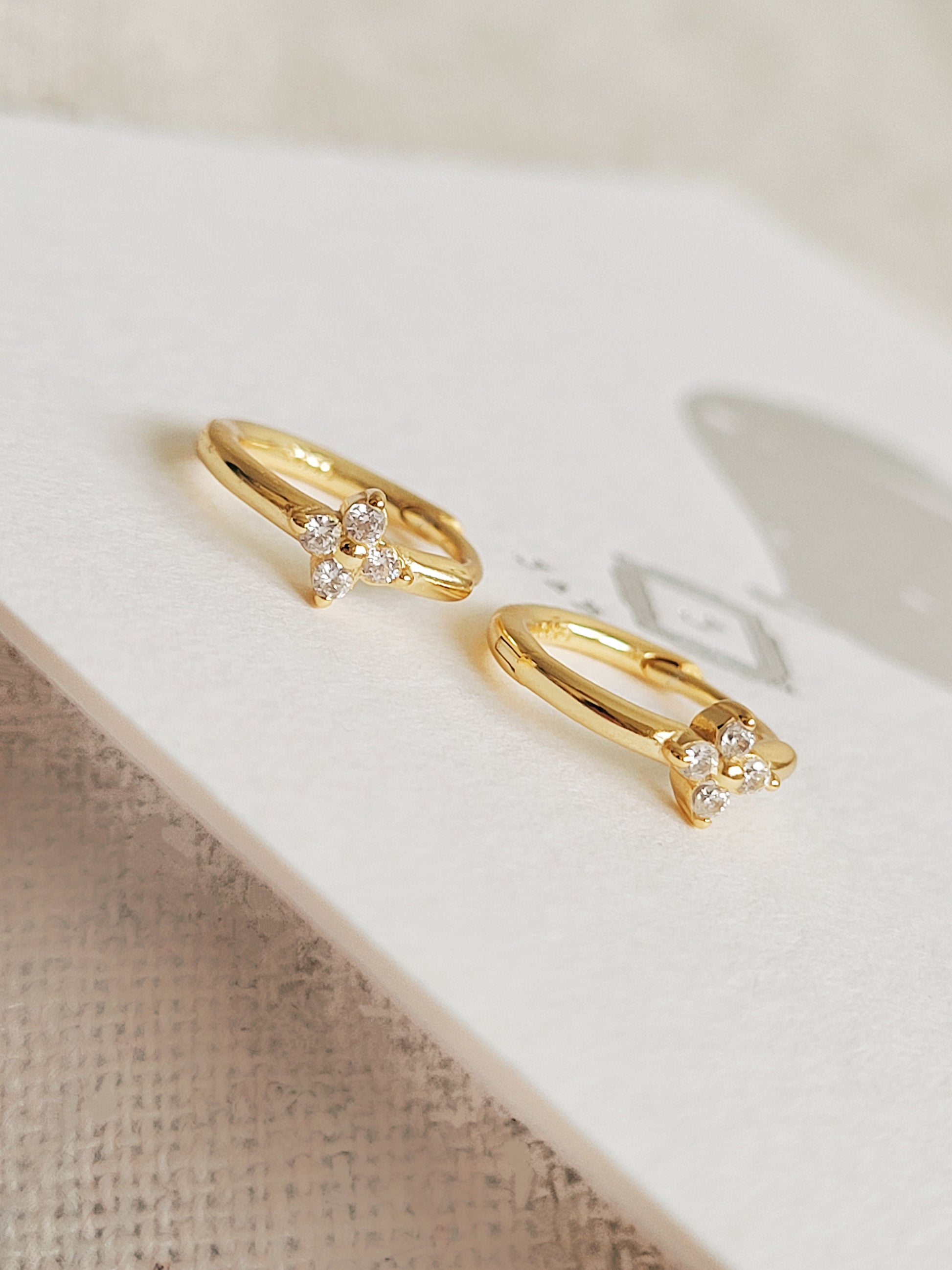 A pair of gold clover earrings displayed on a JaBelle Jewellery card, showcasing it details.