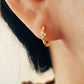 Close up of a woman wearing gold clover huggie earrings, dainty and elegant.