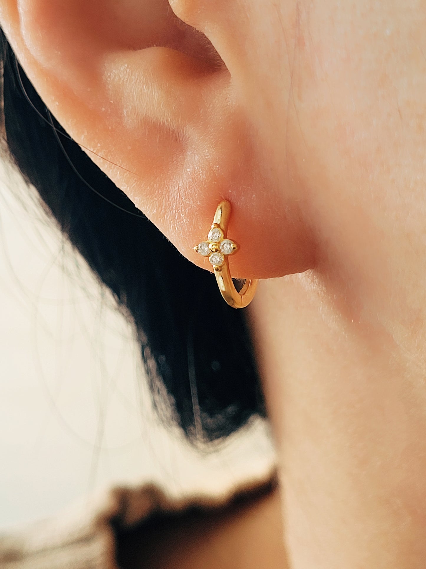 Close up of a woman wearing gold clover huggie earrings, dainty and elegant.