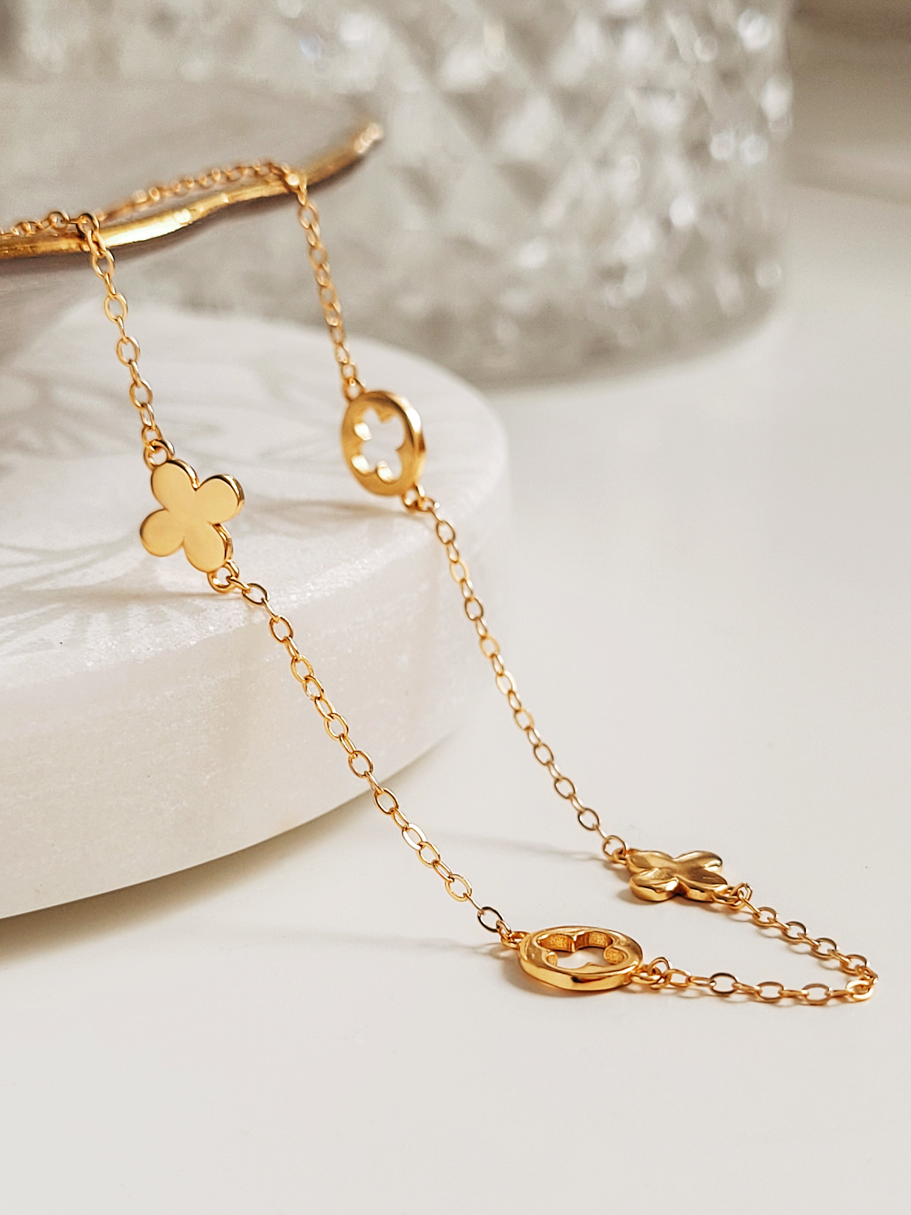 Delicate gold chain necklace with clover-shaped pendants on a white surface.