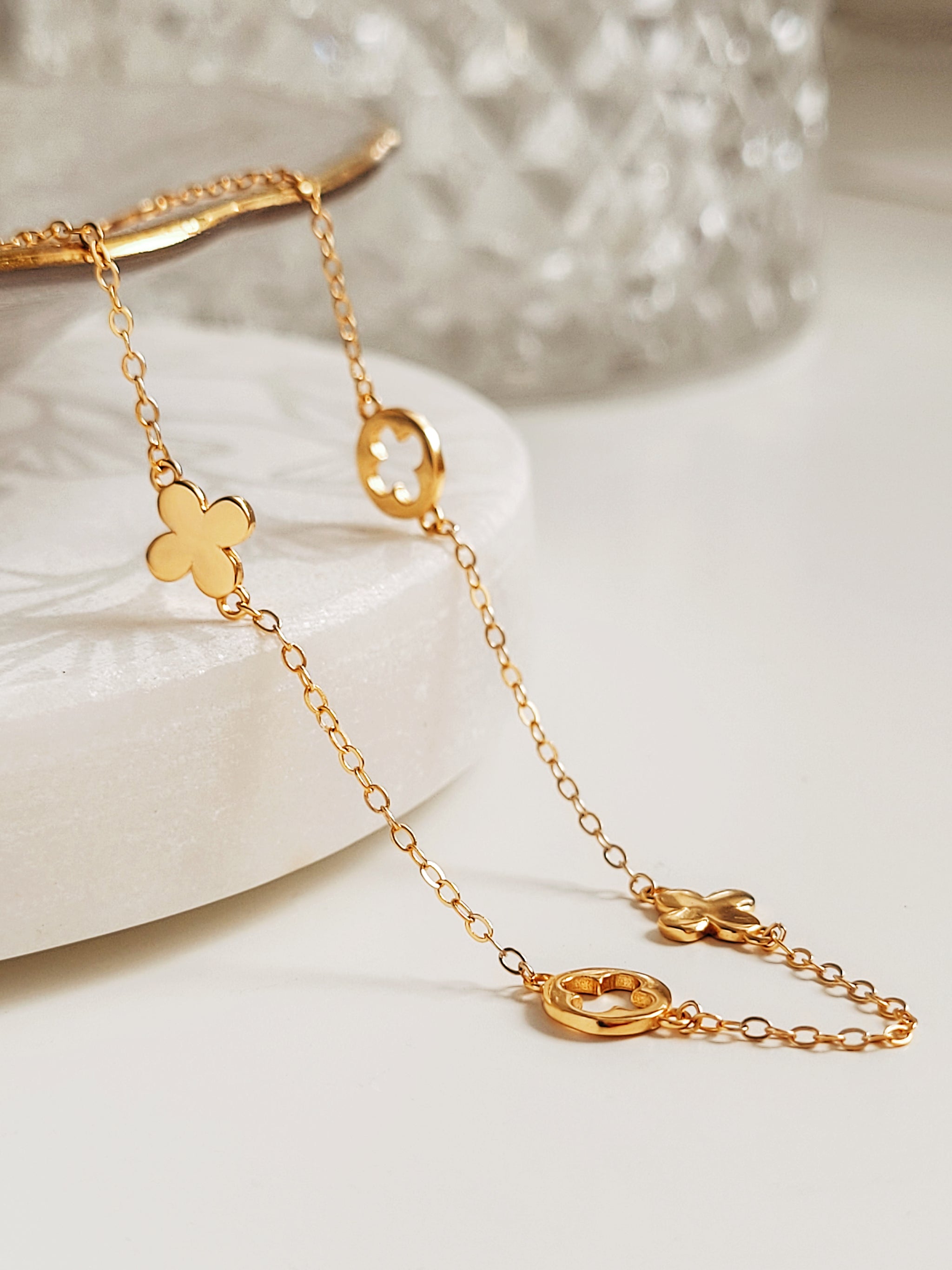 Delicate gold chain necklace with clover-shaped pendants on a white surface.