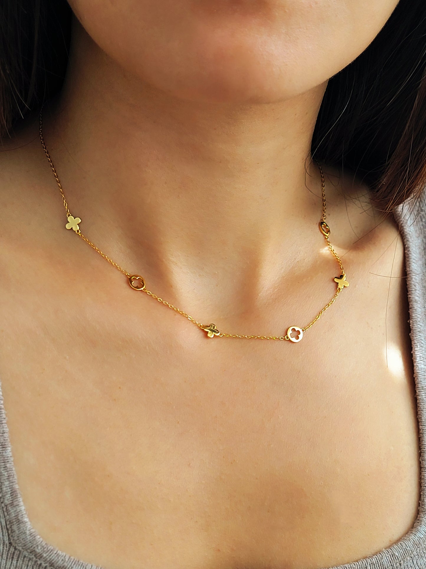 Woman wearing dainty clover necklace crafted in gold plated sterling silver in minimalist and stylish outfit. 