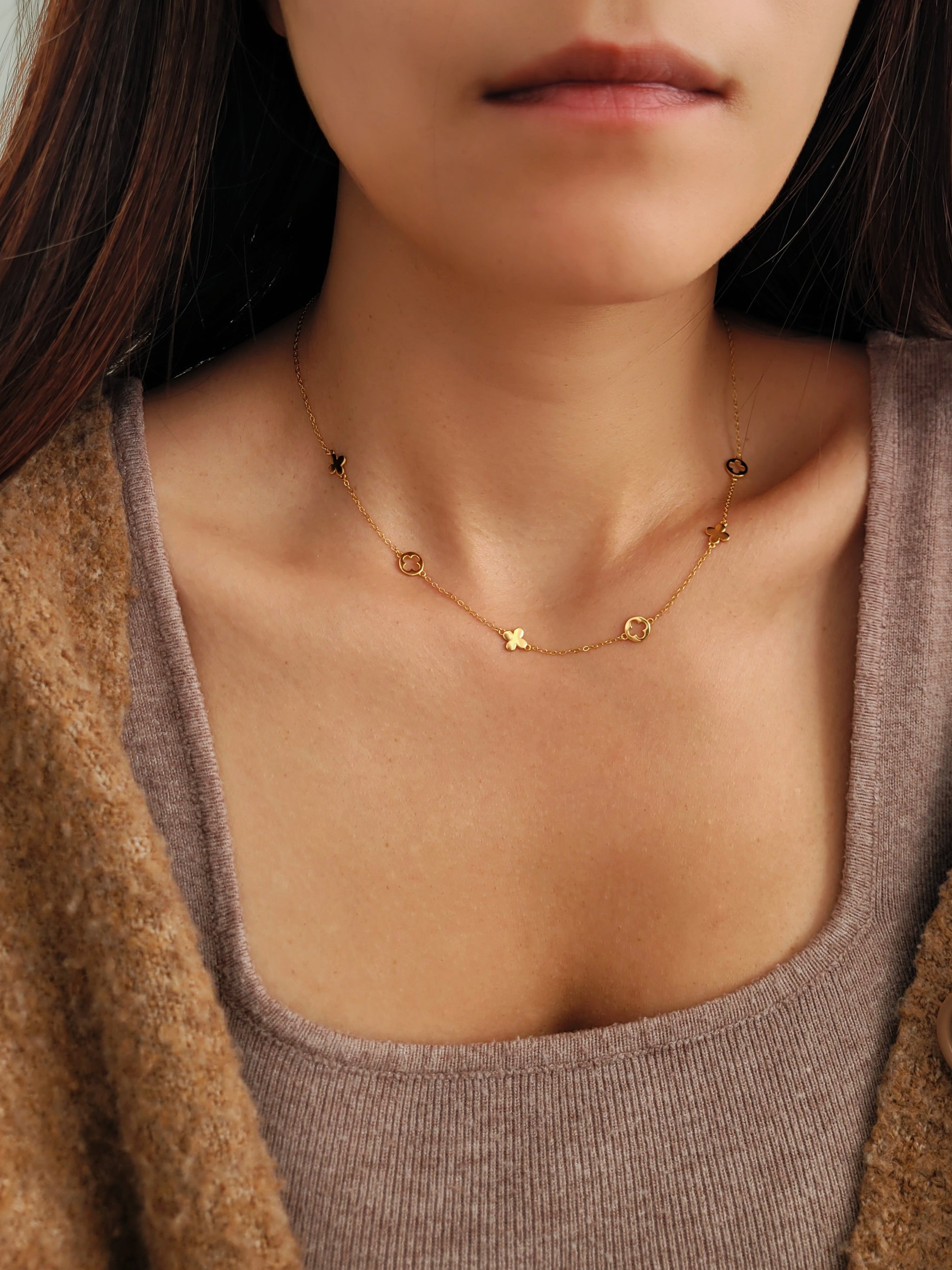 Close-up of a woman wearing a dainty gold necklace with small clover charms.