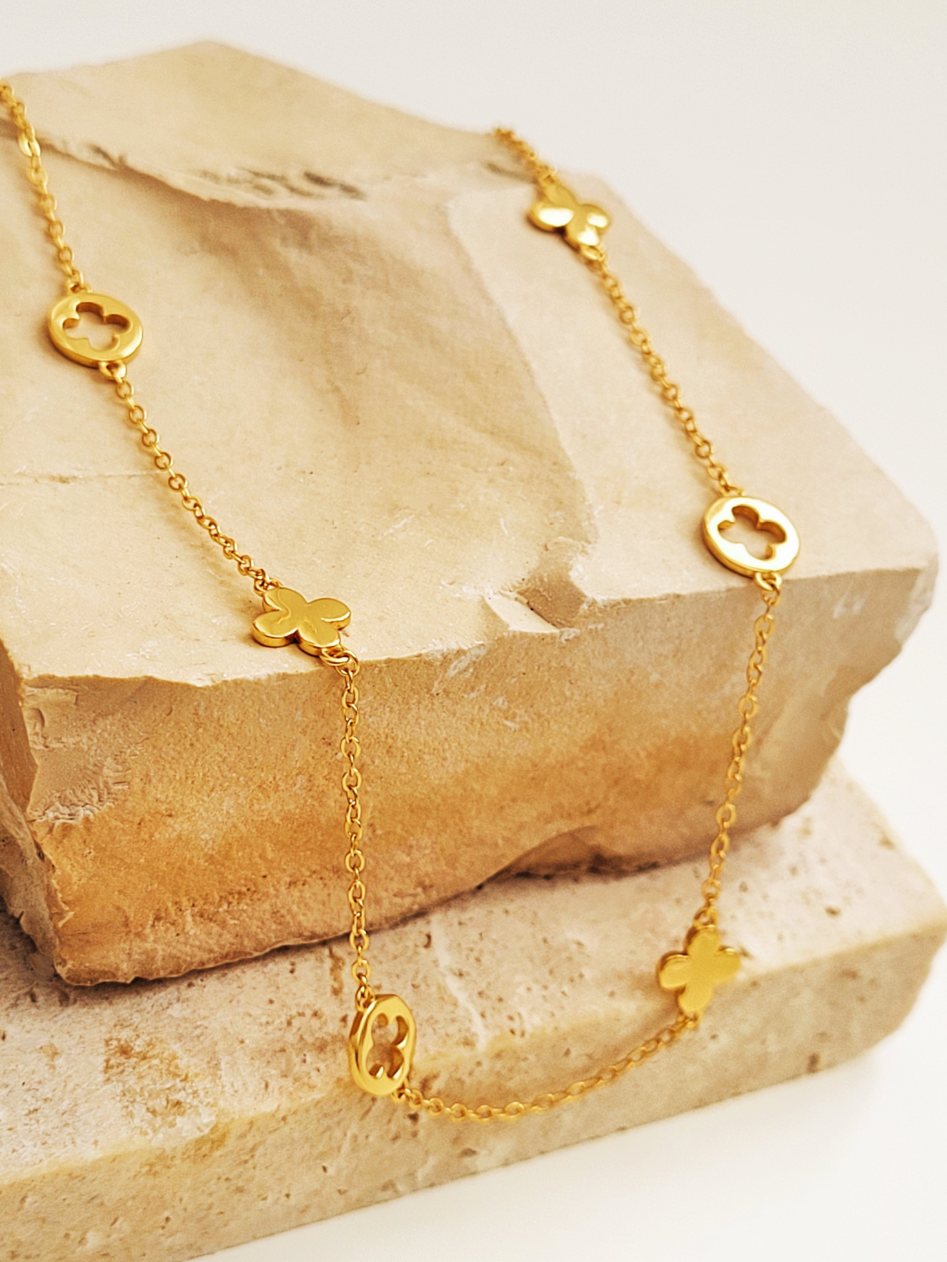 Gold necklace with clover-shaped charms on a stone surface