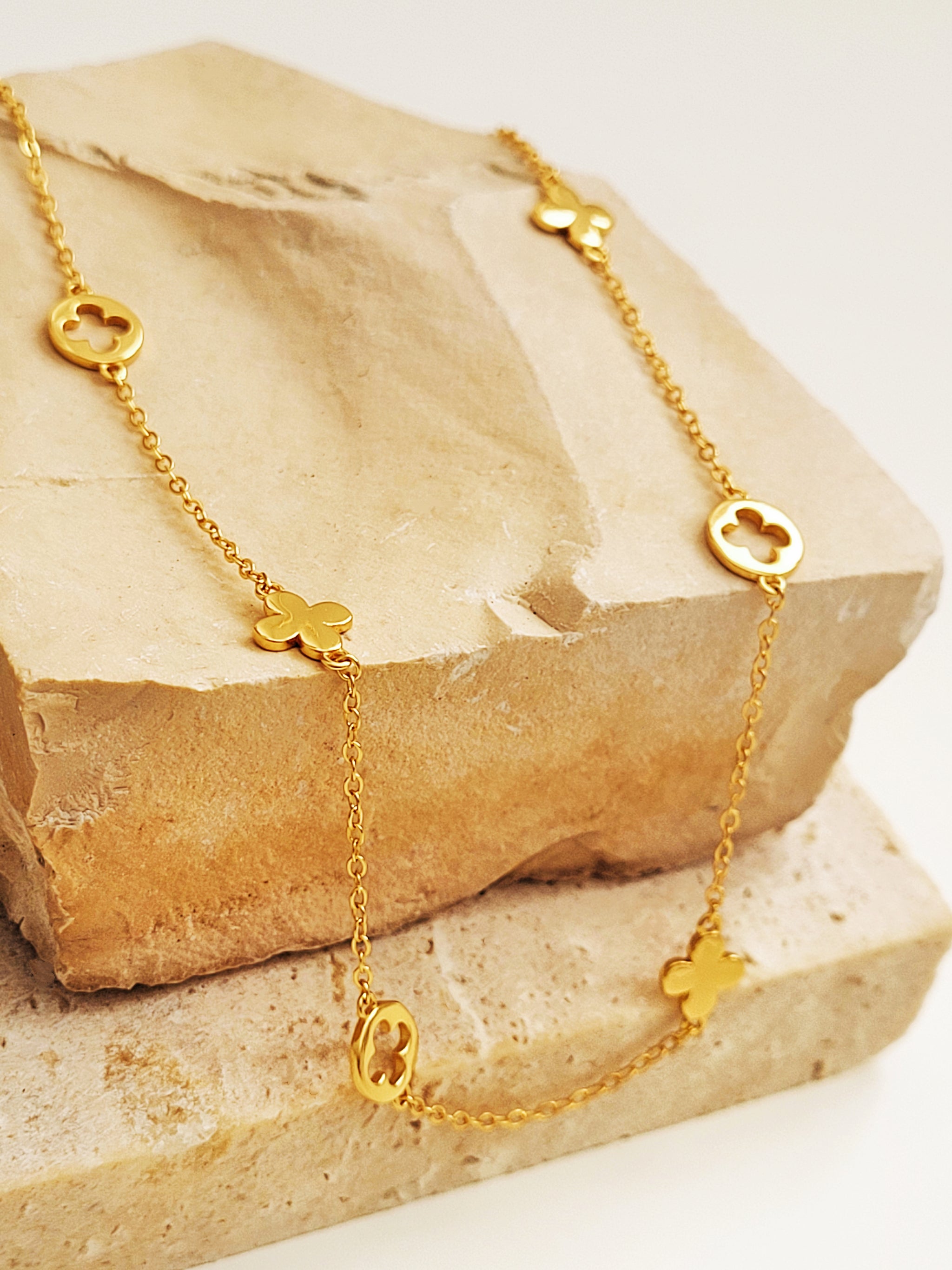 Gold necklace with clover-shaped charms on a stone surface