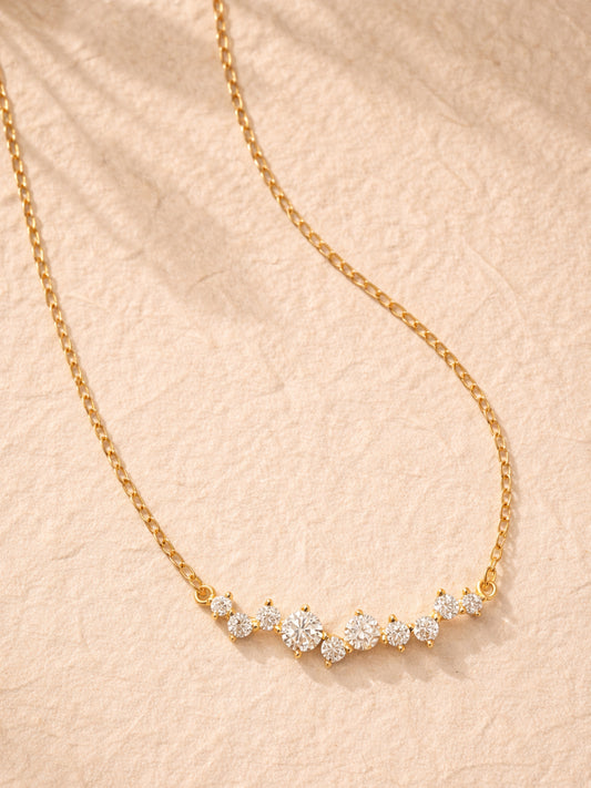 Dainty gold plated sterling silver necklace with cubic zirconia accents on a beige fabric background.