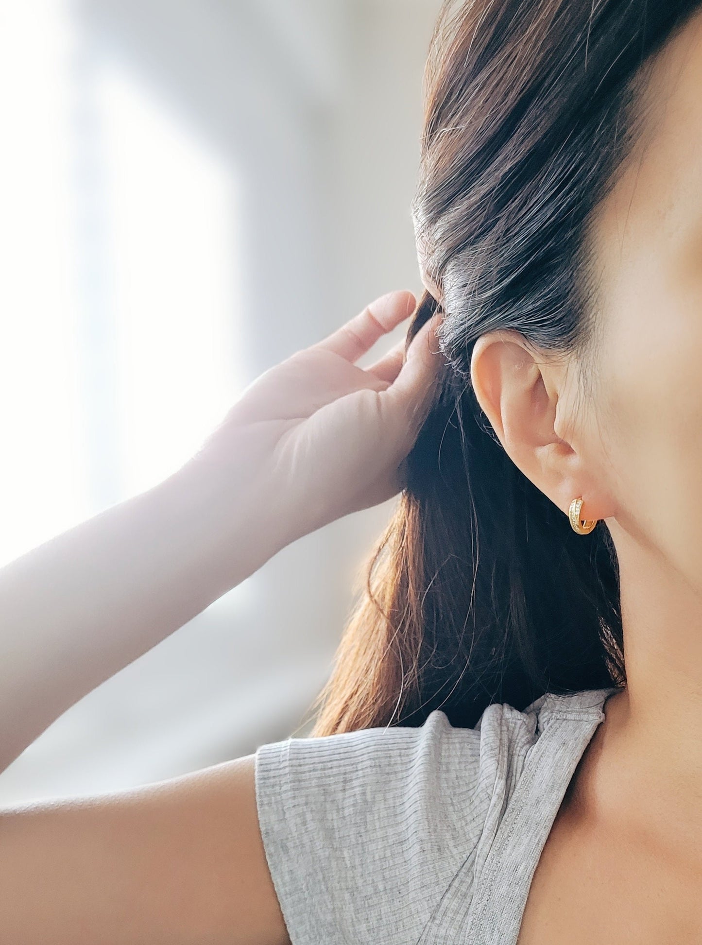 A woman wearing a soft, light-colored sweater, and chic and understated gold crisscross hoop earrings. Emphasizing the minimalistic elegance of the jewelry.