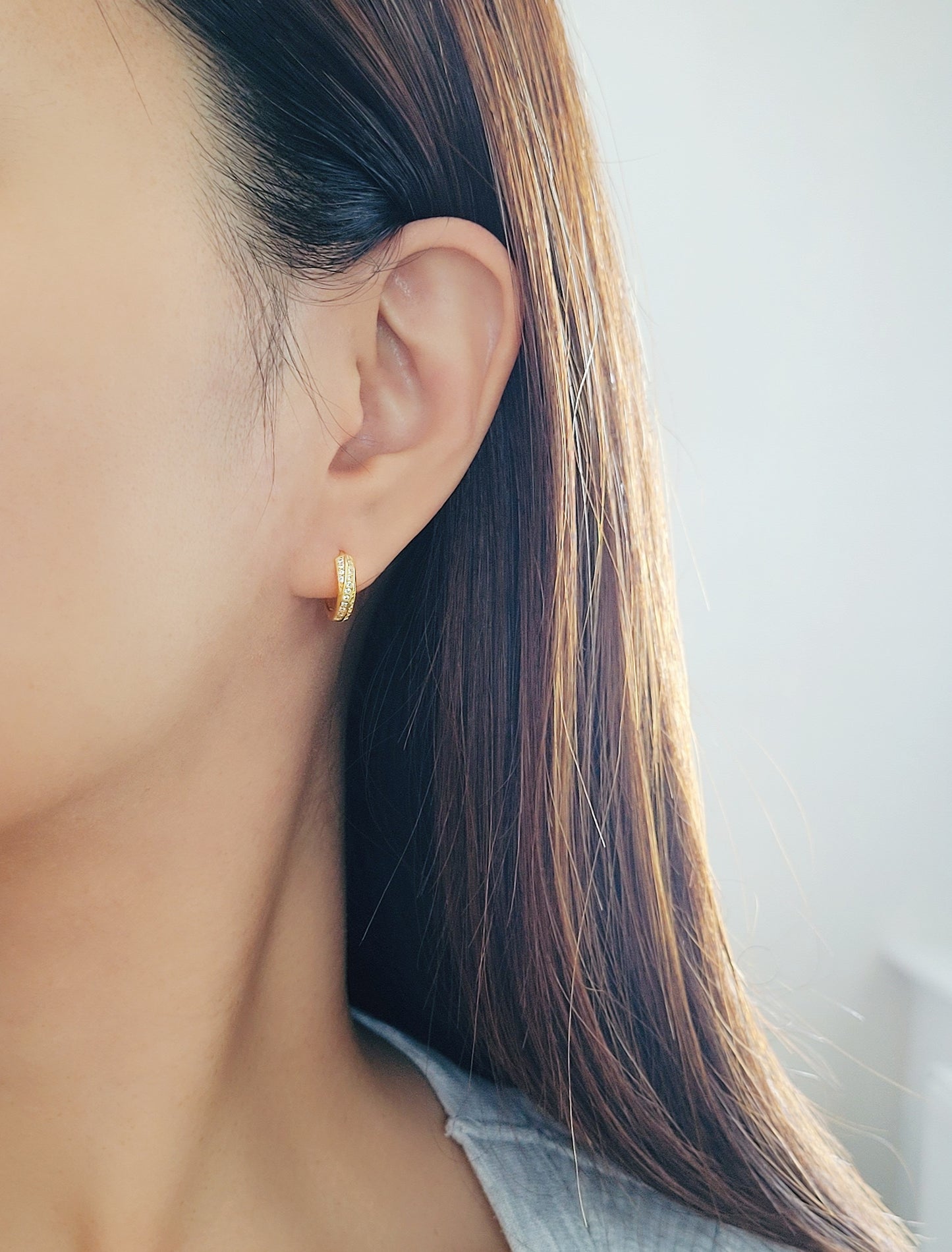 A woman wearing a soft, light-colored sweater, and chic and understated gold crisscross hoop earrings. Emphasizing the minimalistic elegance of the jewelry.