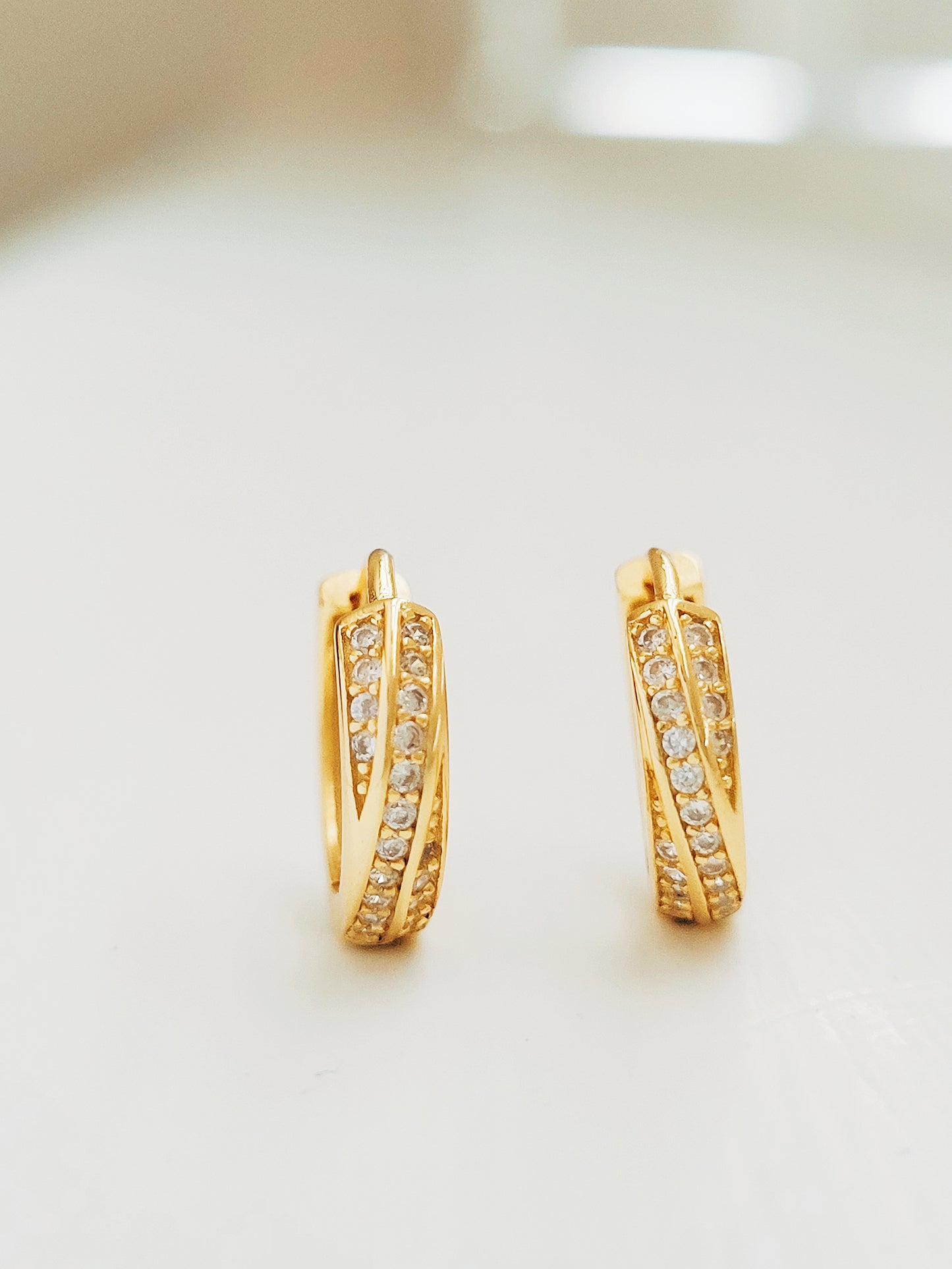 Each gold crisscross hoop showcases two overlapping bands that gracefully intertwine, both encrusted with a row of shimmering zircons, creating a chic, radiant design.