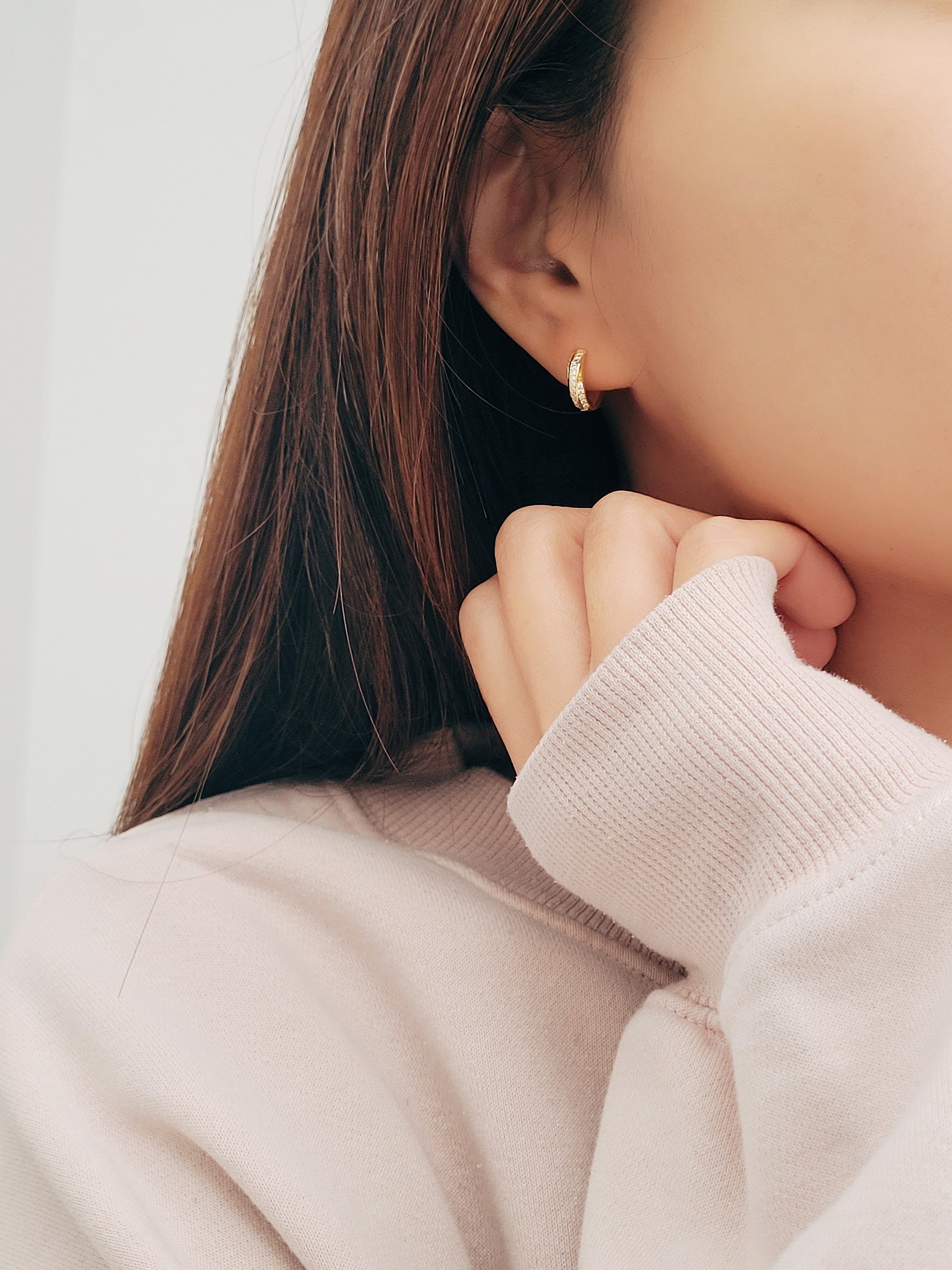 A woman wearing a soft, light-colored sweater, and chic and understated gold crisscross hoop earrings. Emphasizing the minimalistic elegance of the jewelry.