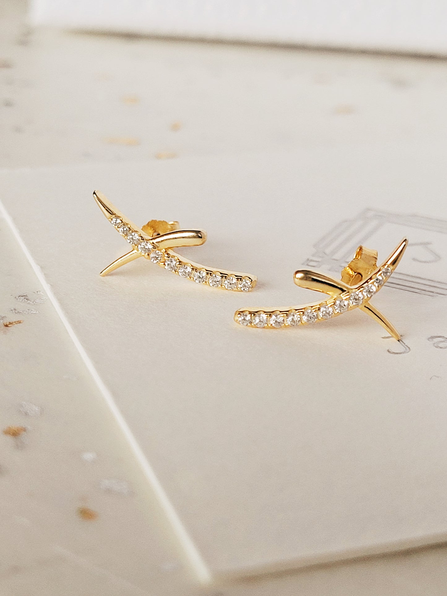 A pair of gold cross stud earrings with cubic zirconia stones displayed on an elegant white surface