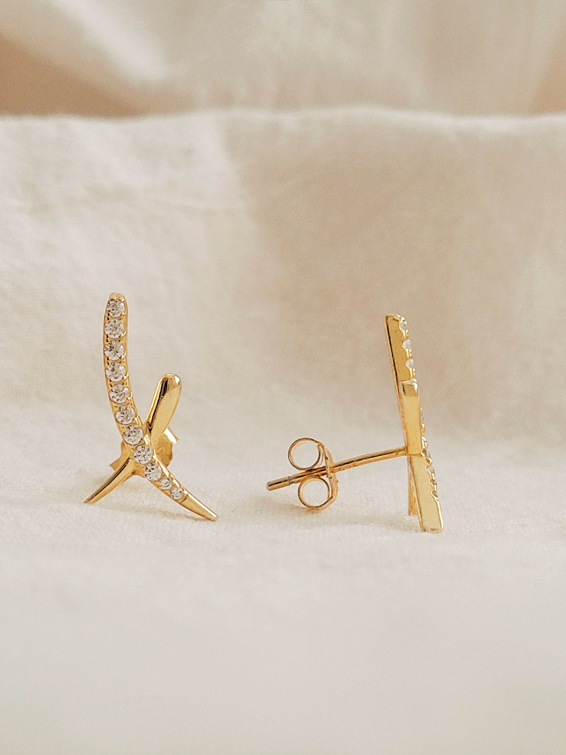 A pair of gold cross stud earrings with cubic zirconia stones displayed on an elegant white surface