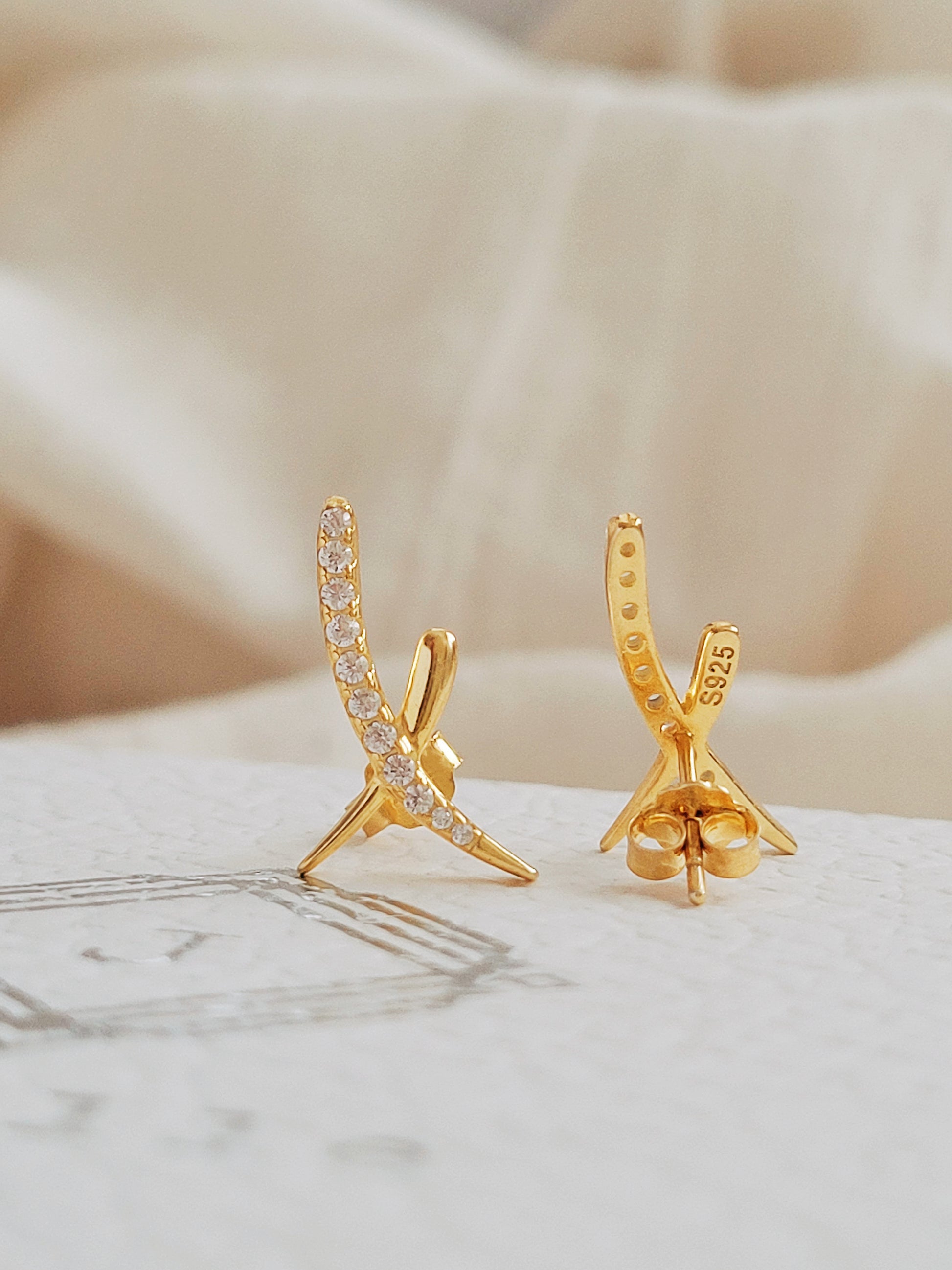 A pair of gold X stud earrings with cubic zirconia stones displayed on an elegant white surface