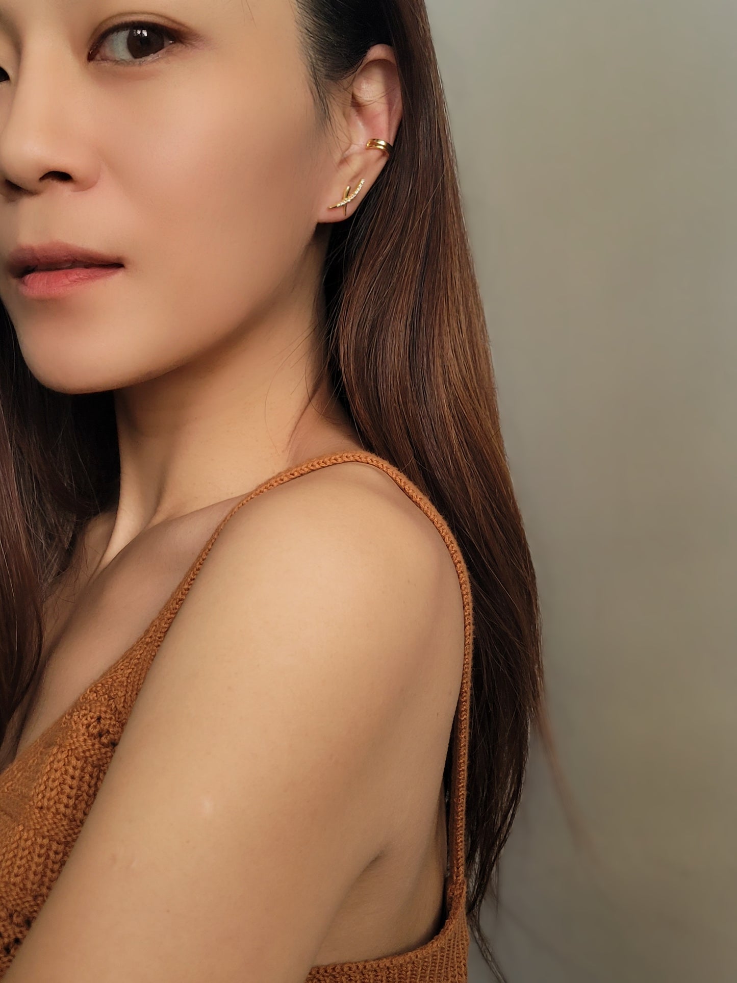 A woman wearing gold cross ear climber earrings with sparkling cubic zirconia and pair with a double layer ear cuff, showcasing her elegant and minimalist style.