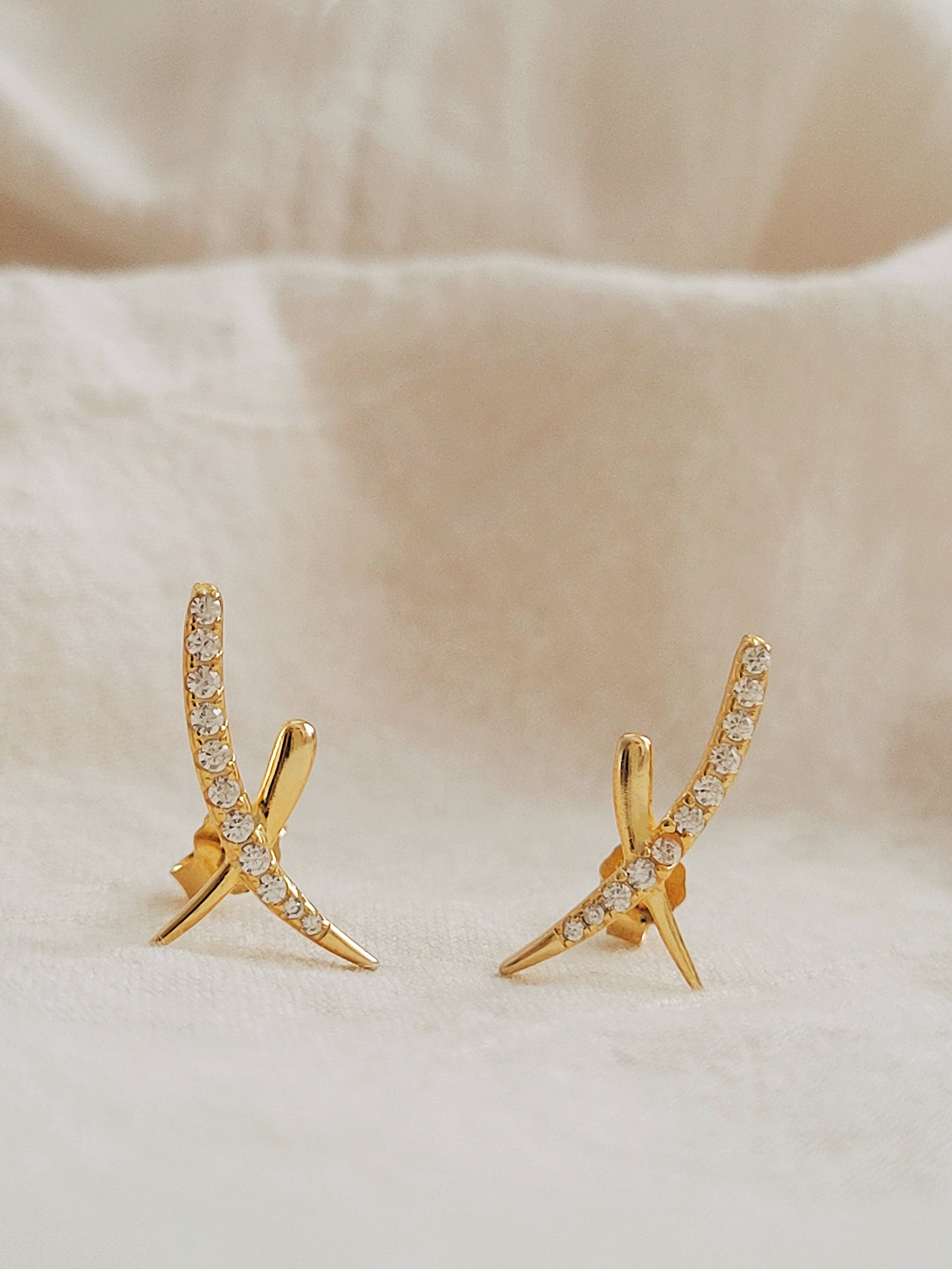 A pair of gold cross stud earrings with cubic zirconia stones displayed on an elegant white surface