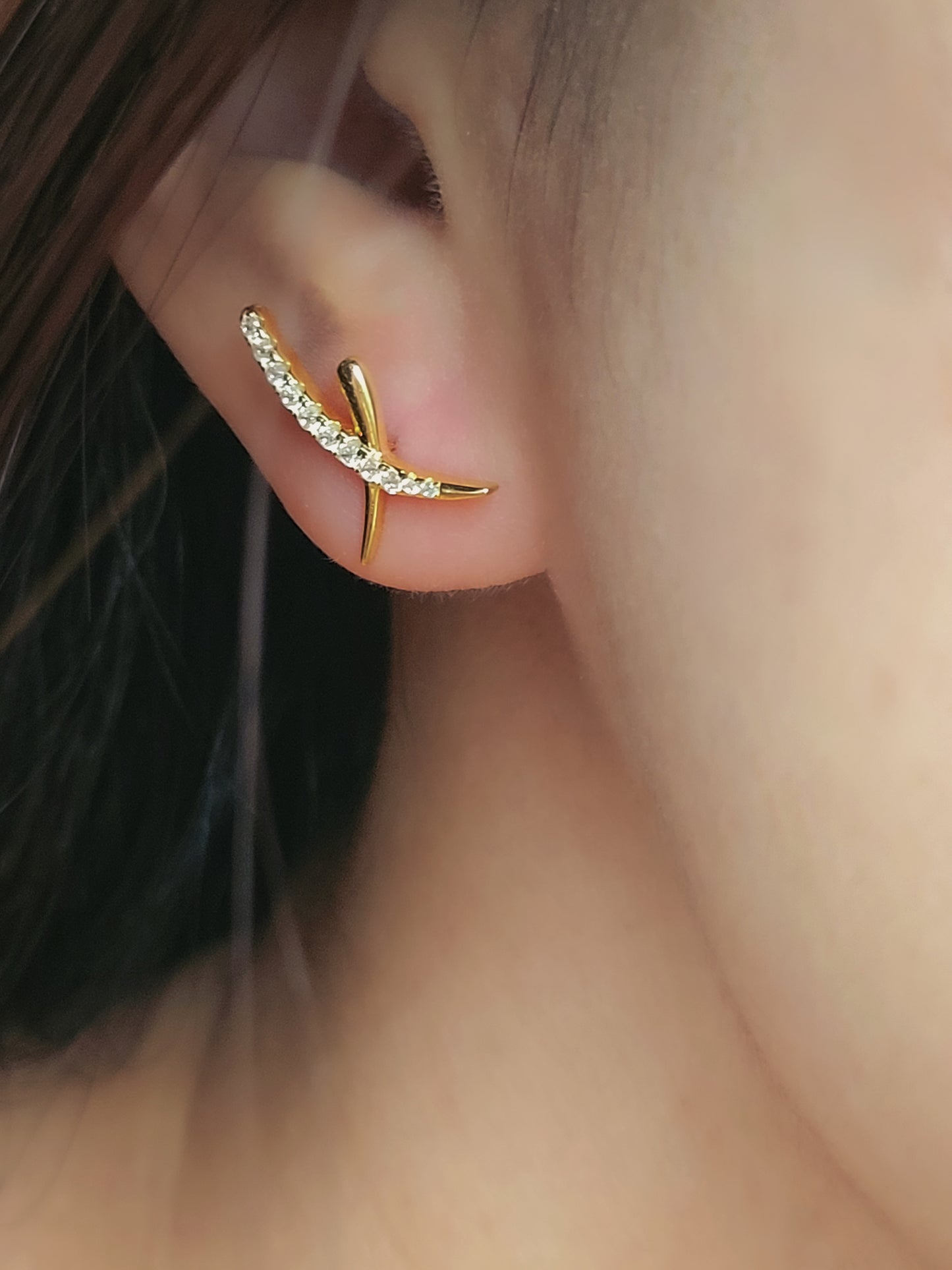 A close-up of a woman wearing gold cross ear climber earrings with sparkling cubic zirconia stones.