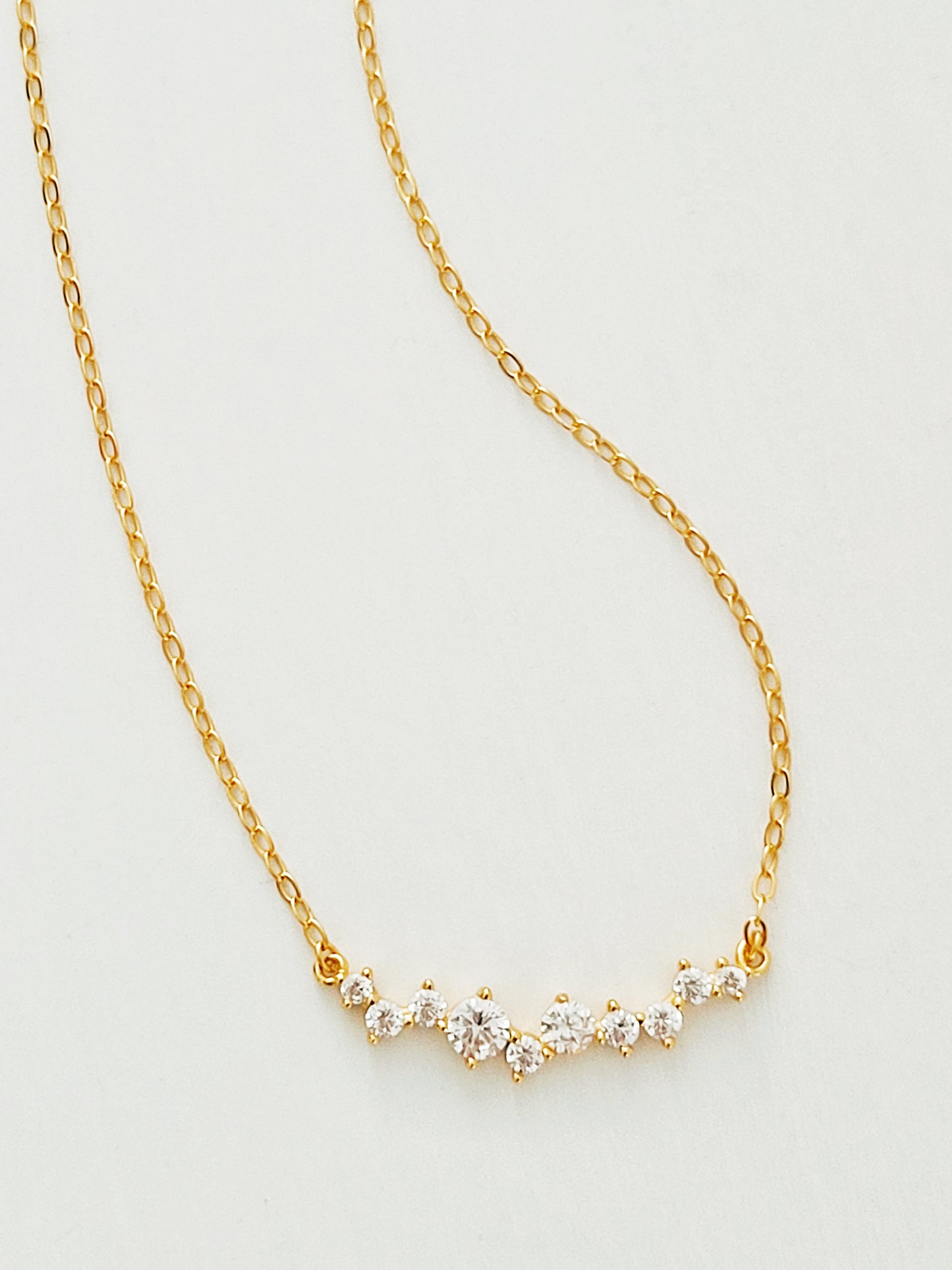 Close-up of a dainty gold necklace with curved cubic zirconia pendant, perfect anniversary gift for her.