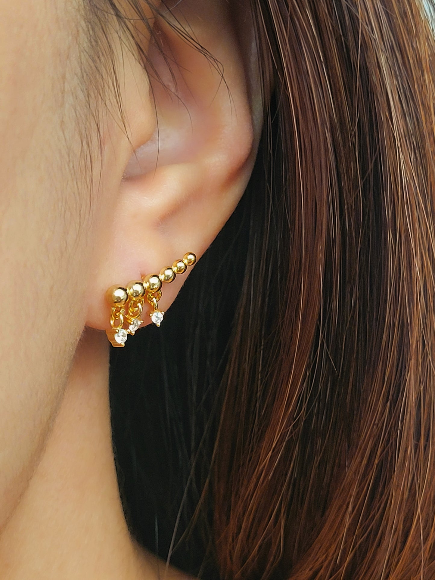 A woman wearing a dainty gold ear crawler designed with three tiny diamond drops, featuring a trendy and chic design perfect for everyday wear or special occasions.