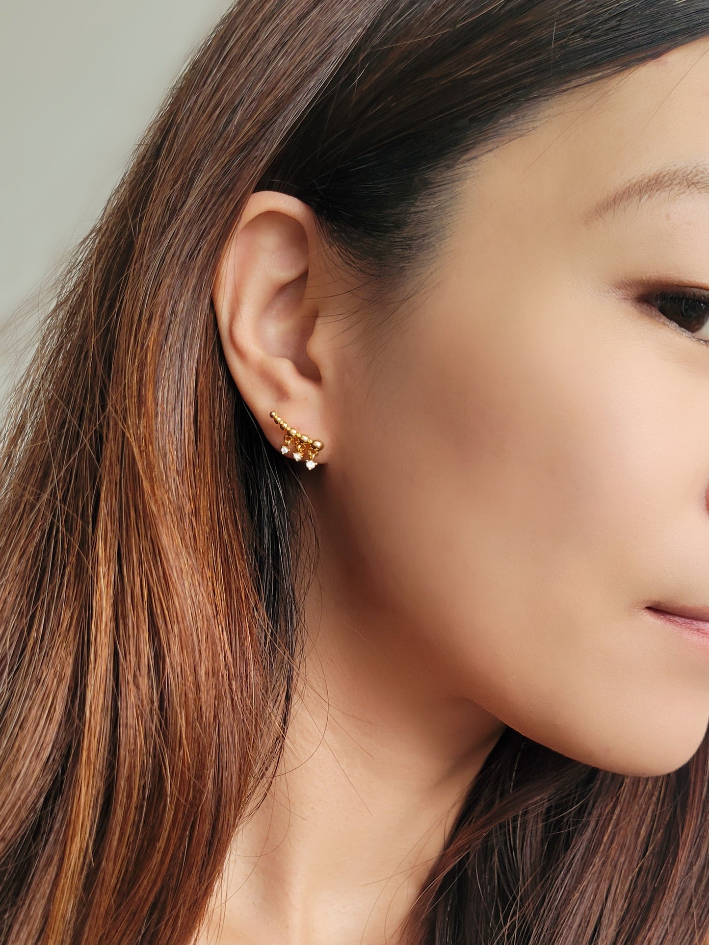 A woman wearing a dainty gold ear crawler designed with three tiny diamond drops, featuring a trendy and chic design perfect for everyday wear or special occasions.