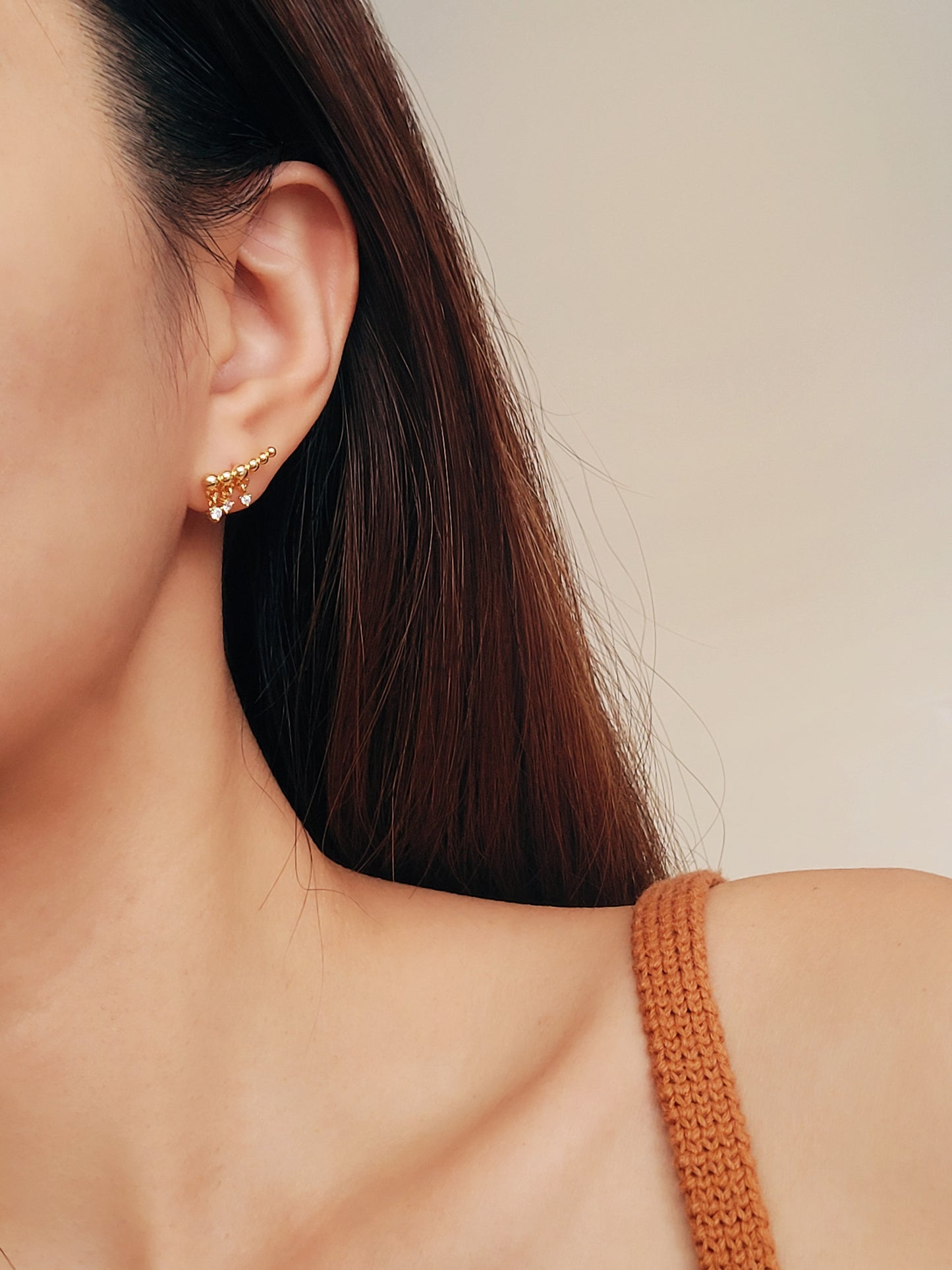 A woman wearing a dainty gold ear crawler designed with three tiny diamond drops, featuring a trendy and chic design perfect for everyday wear or special occasions.