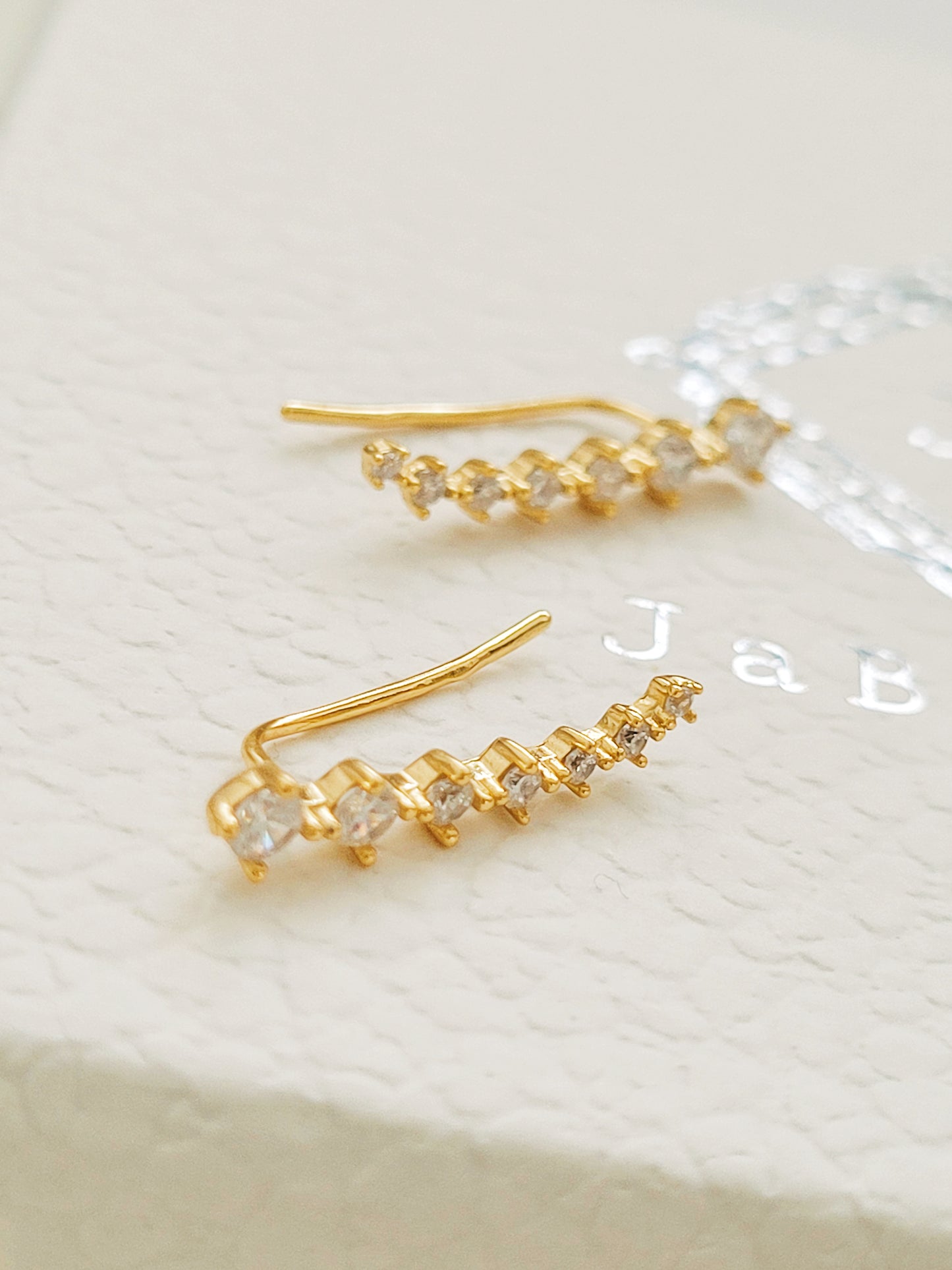 A pair of gold-plated sterling silver climber earrings adorned with cubic zirconia stones, displayed on a clean white surface.