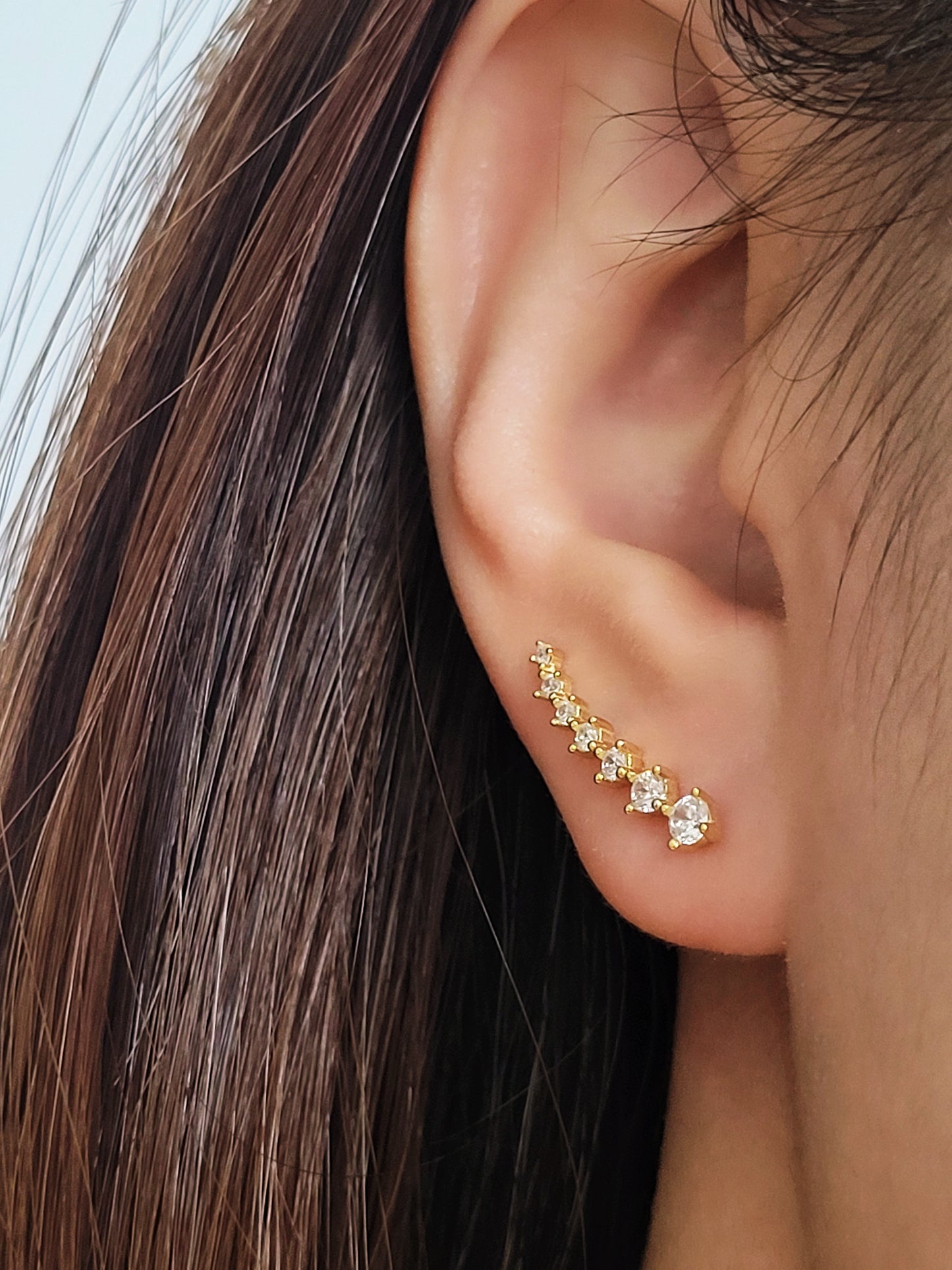 Close-up of a woman&#39;s ear wearing an 18K gold-plated cubic zirconia climber earring, highlighting the elegant and minimalist design.