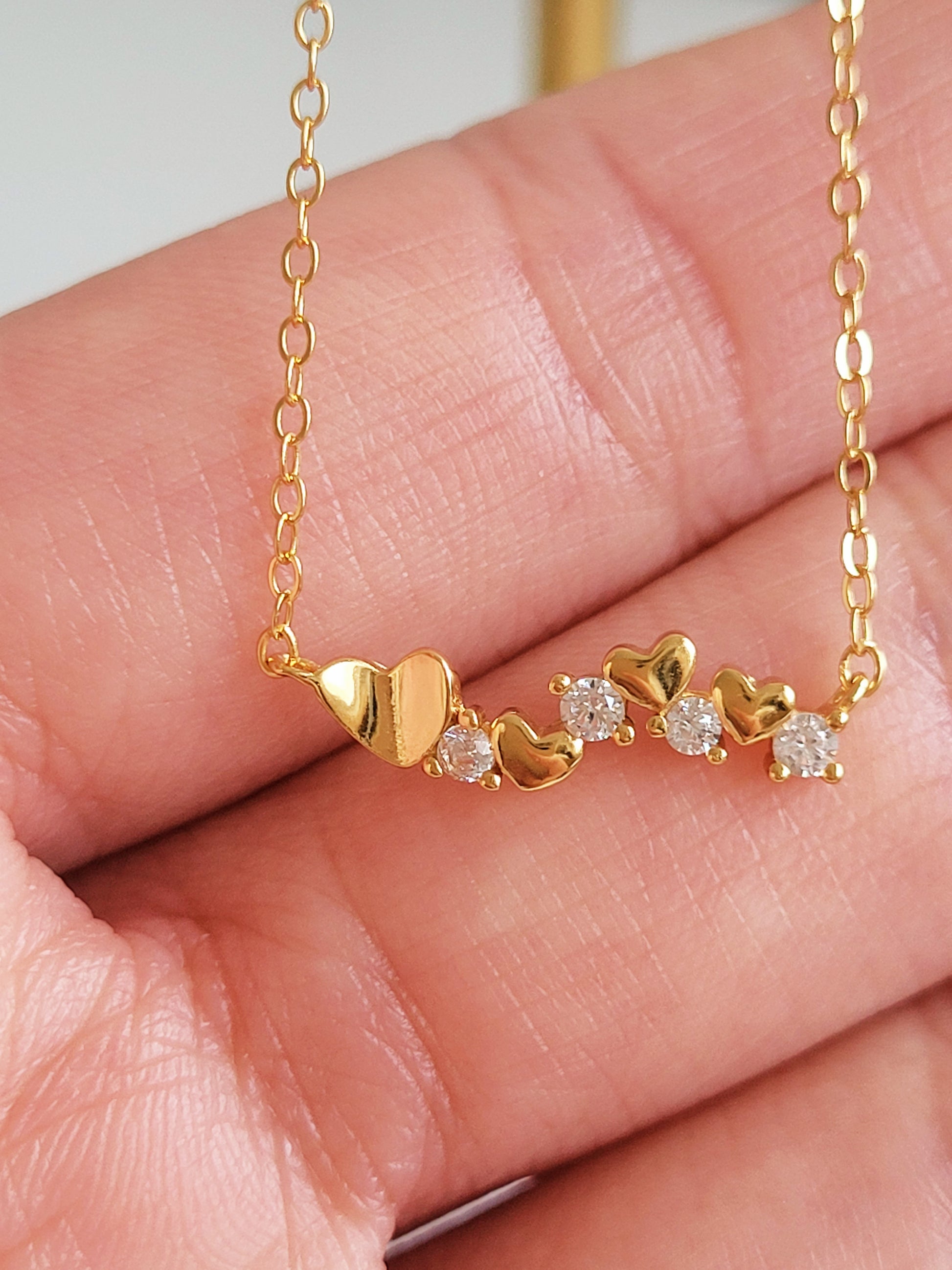 Close-up of a dainty gold necklace with heart charms and sparkling diamond accents, perfect for weddings, bridal showers, and Valentine’s Day.