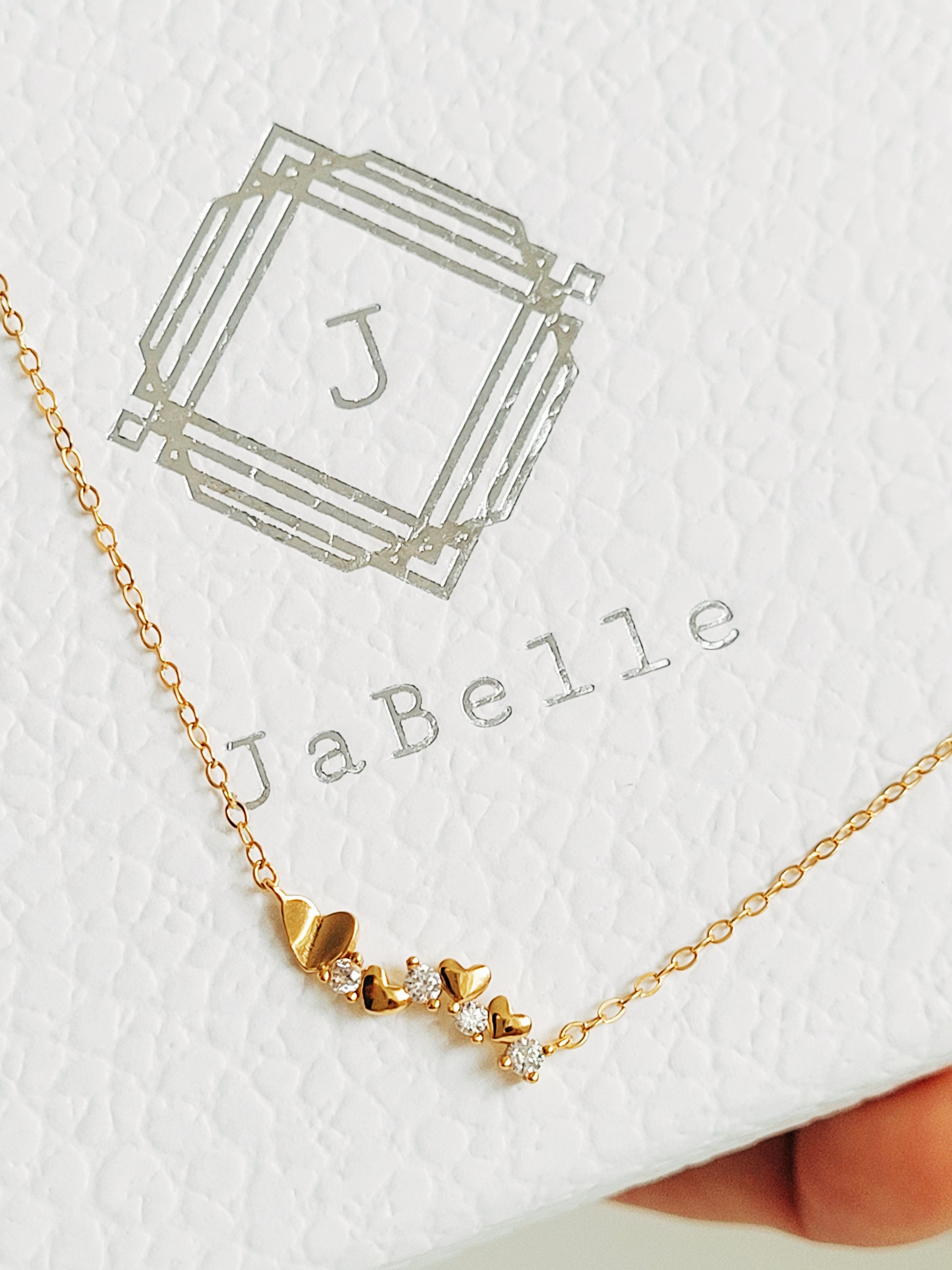 Close-up of a dainty gold necklace with heart charms and sparkling diamond accents, perfect for weddings, bridal showers, and Valentine’s Day.