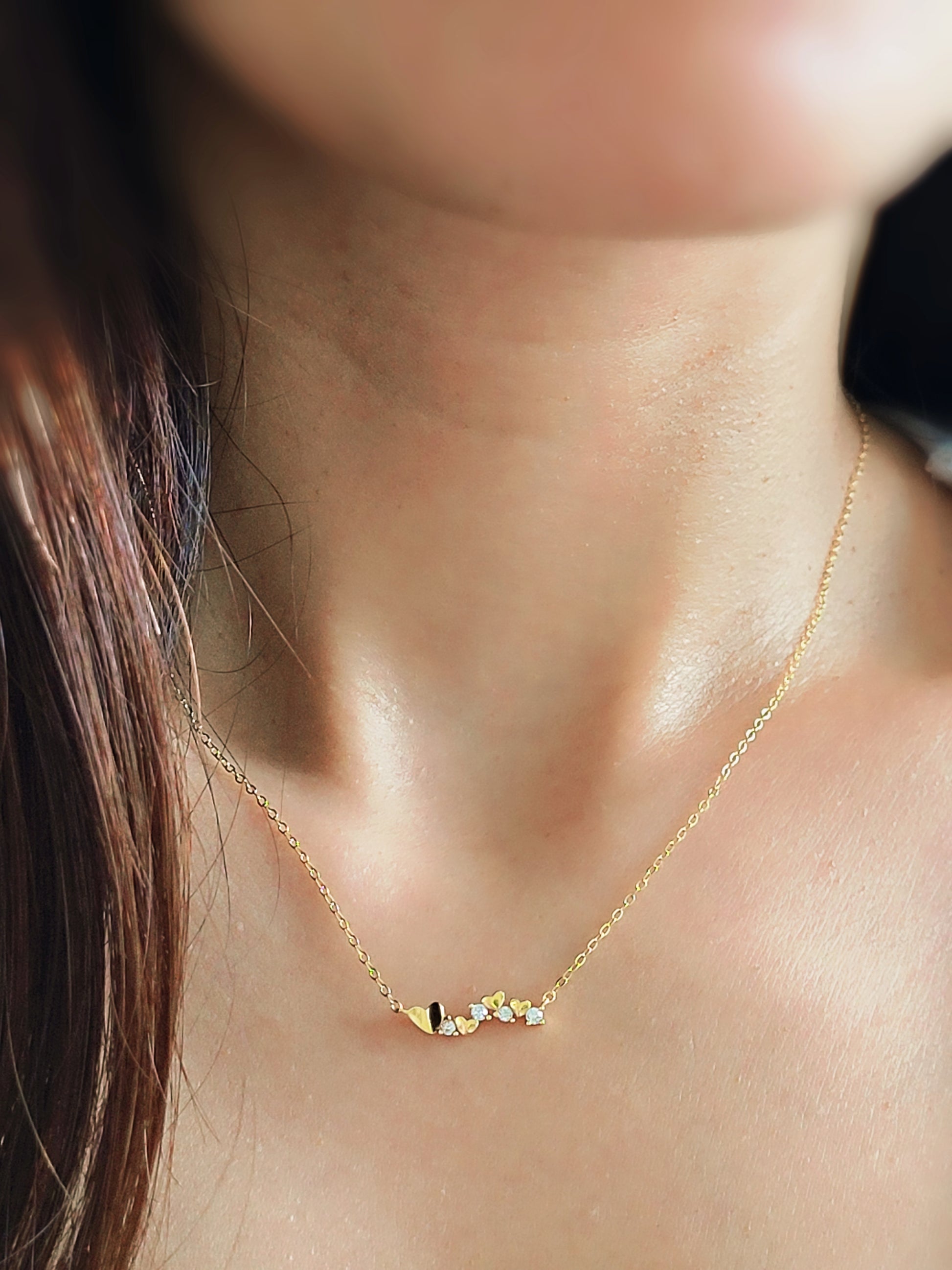 Close-up of a dainty gold necklace with heart charms and sparkling diamond accents, worn on a woman’s neck, perfect for weddings, bridal showers, and Valentine’s Day.