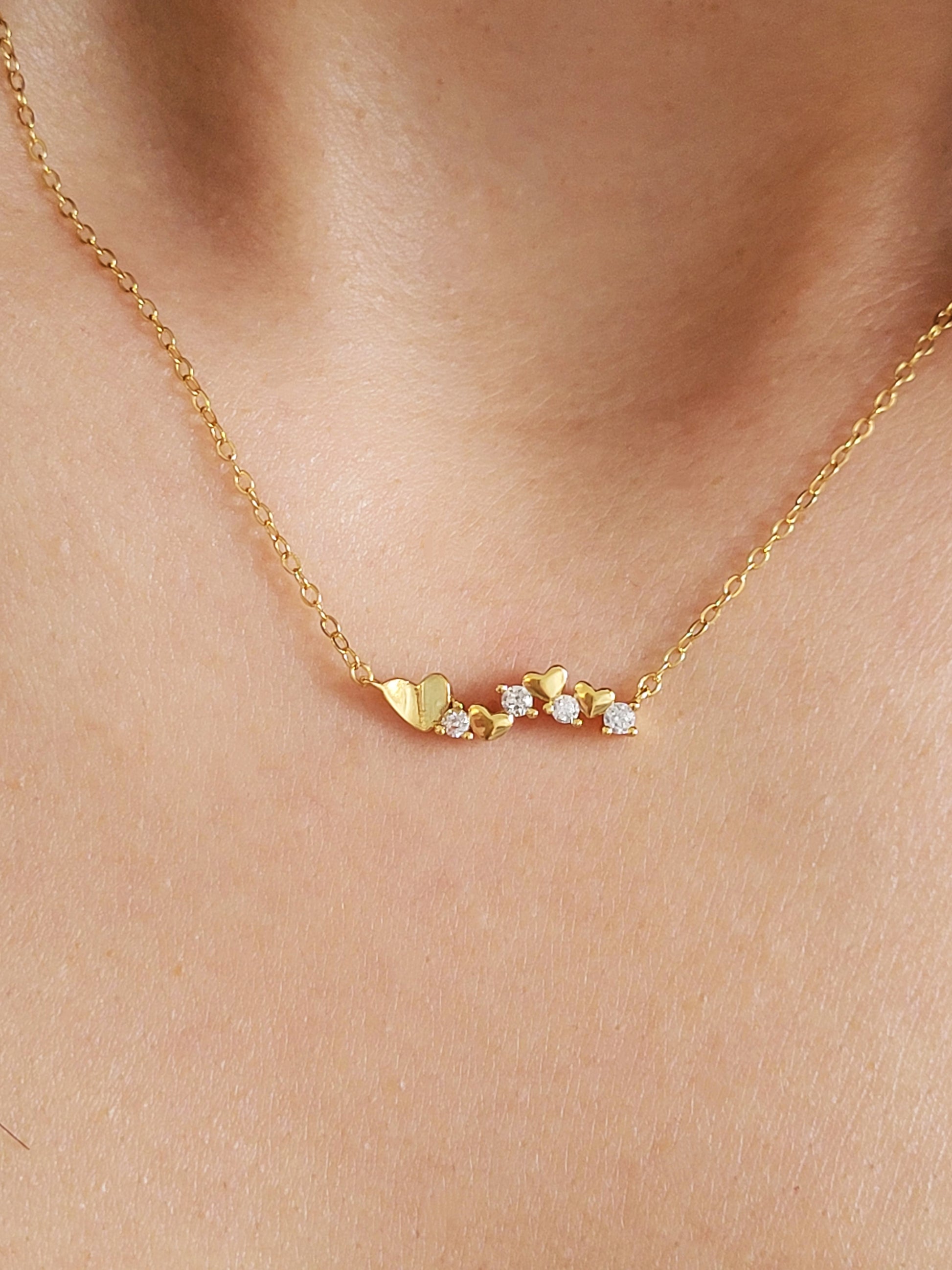 Close-up of a dainty gold necklace with heart charms and sparkling diamond accents, worn on a woman’s neck, perfect for weddings, bridal showers, and Valentine’s Day.