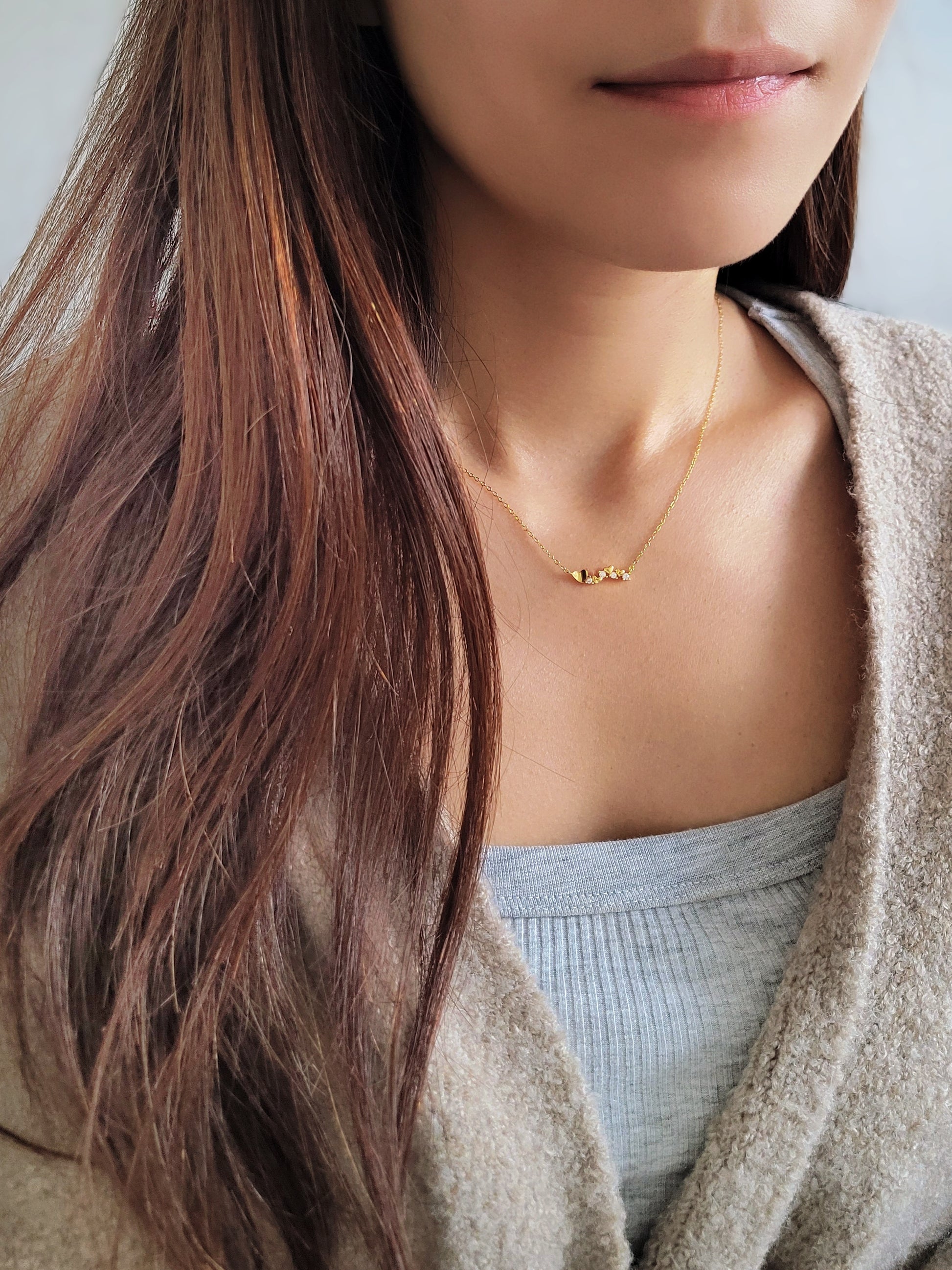 Close-up of a dainty gold necklace with heart charms and sparkling diamond accents, worn on a woman’s neck, perfect for weddings, bridal showers, and Valentine’s Day.