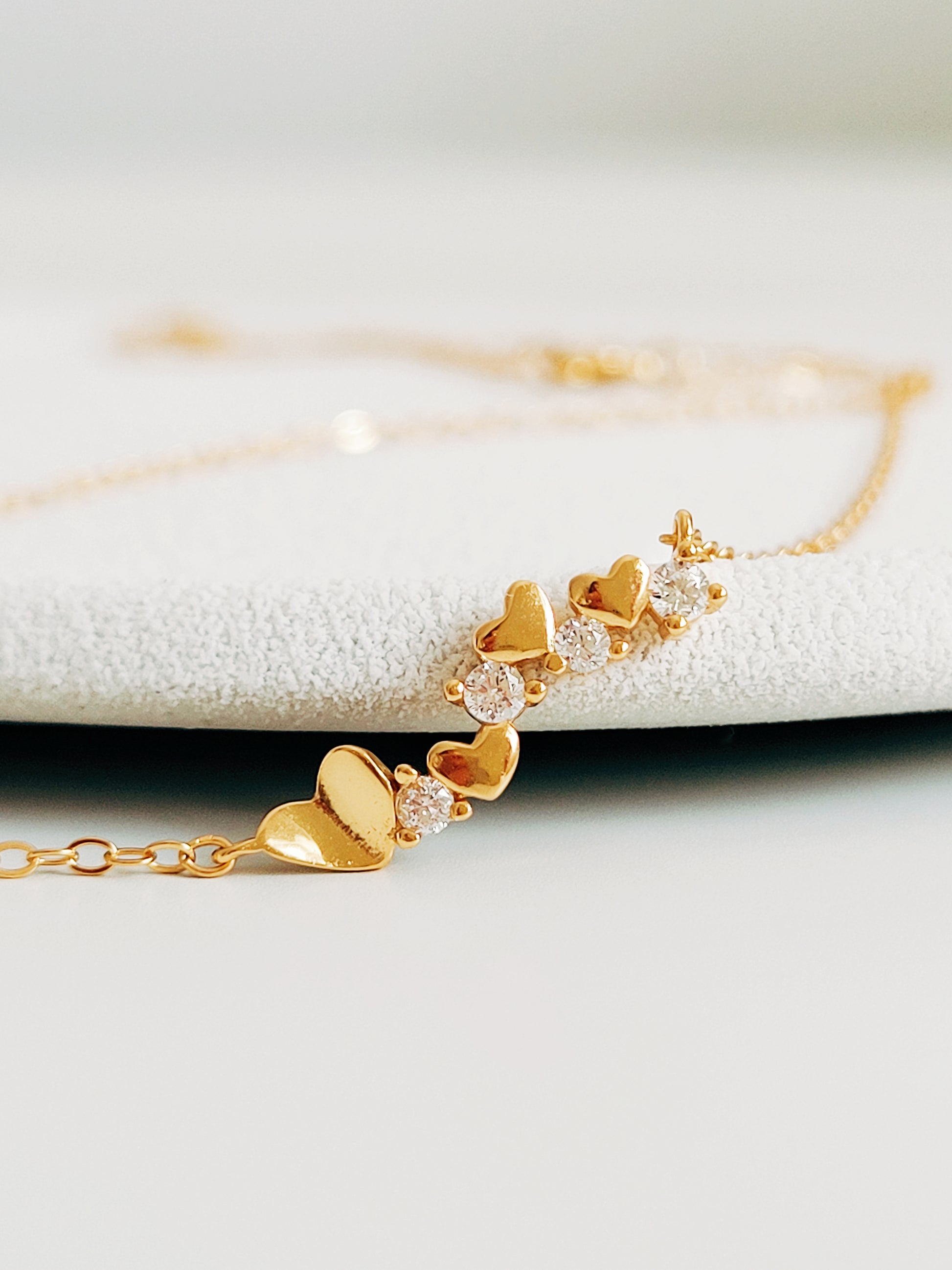 Close-up of a dainty gold necklace with heart charms and sparkling diamond accents, perfect for weddings, bridal showers, and Valentine’s Day.