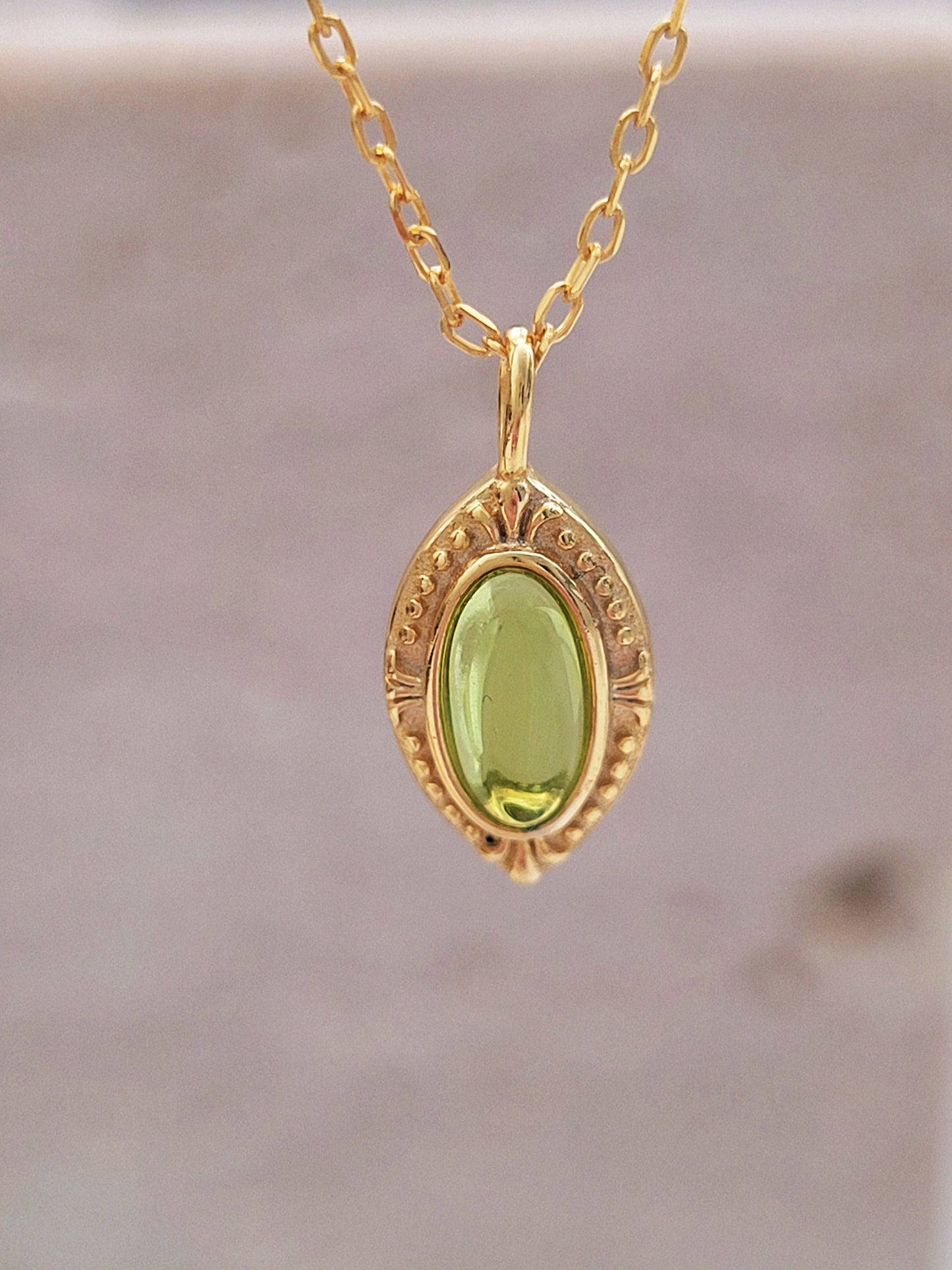 Chic and timeless gold necklace showcasing a vivid green gemstone centerpiece in an ornate oval setting.