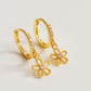 A pair of dainty gold huggie earrings with delicate flower charms on a white surface.