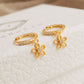 A pair of dainty gold huggie earrings featuring dangly flower charm displayed on a jewellery box. 