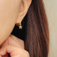 Woman wearing a cute gold plated sterling silver huggie earrings with a flower charm dangle.