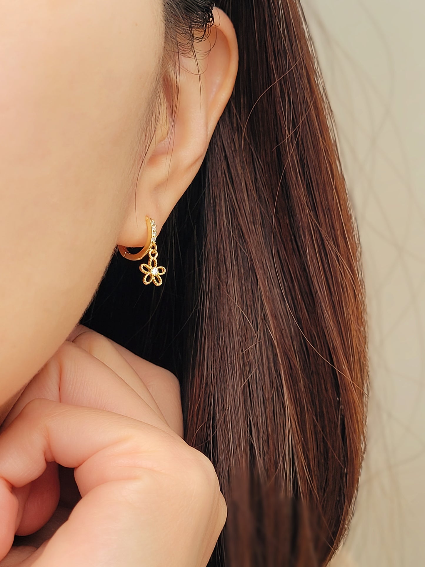 Woman wearing a cute gold plated sterling silver huggie earrings with a flower charm dangle.
