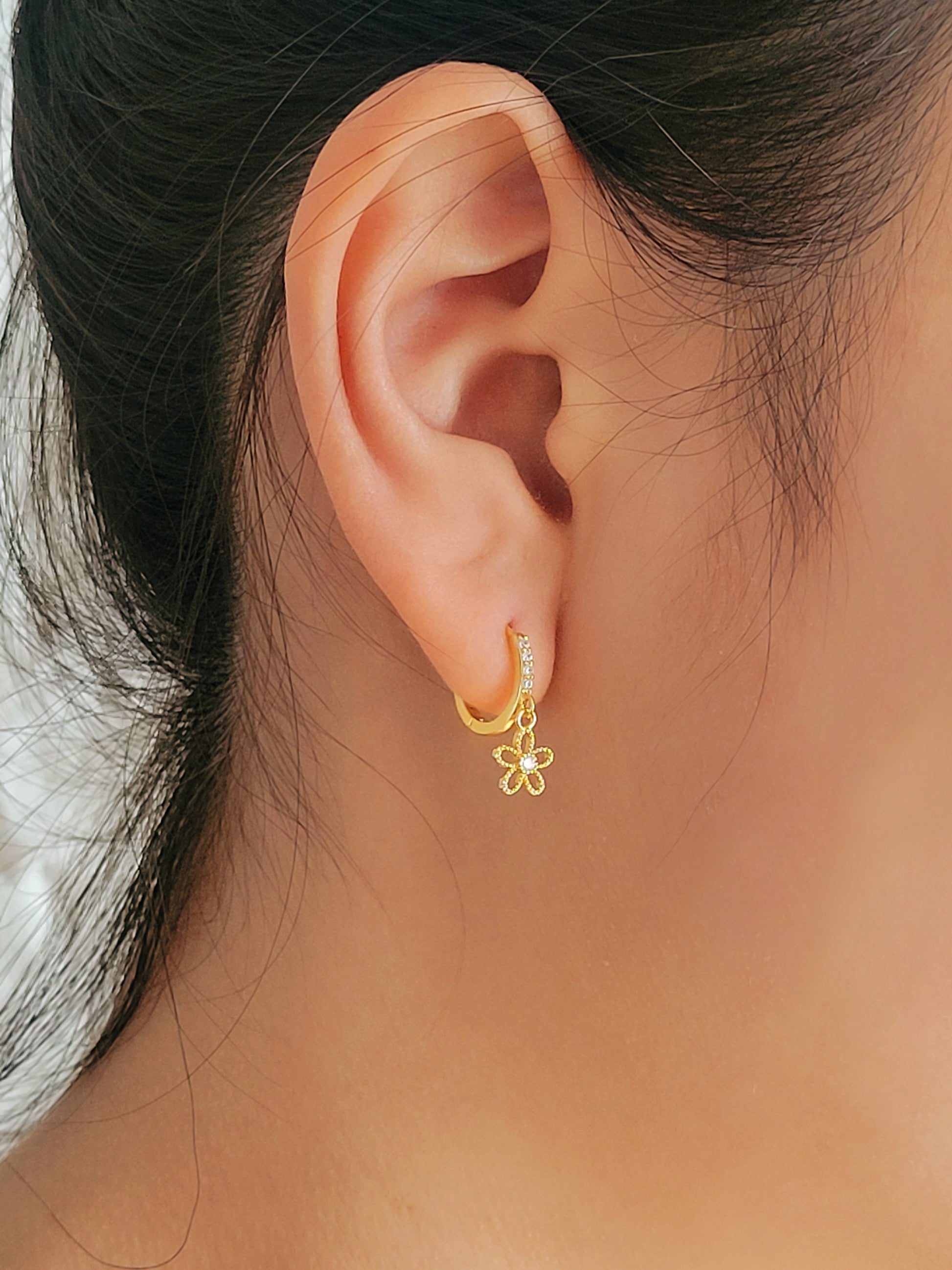 Side view of a beautiful flower earrings on huggie hoops worn on a woman's ear.