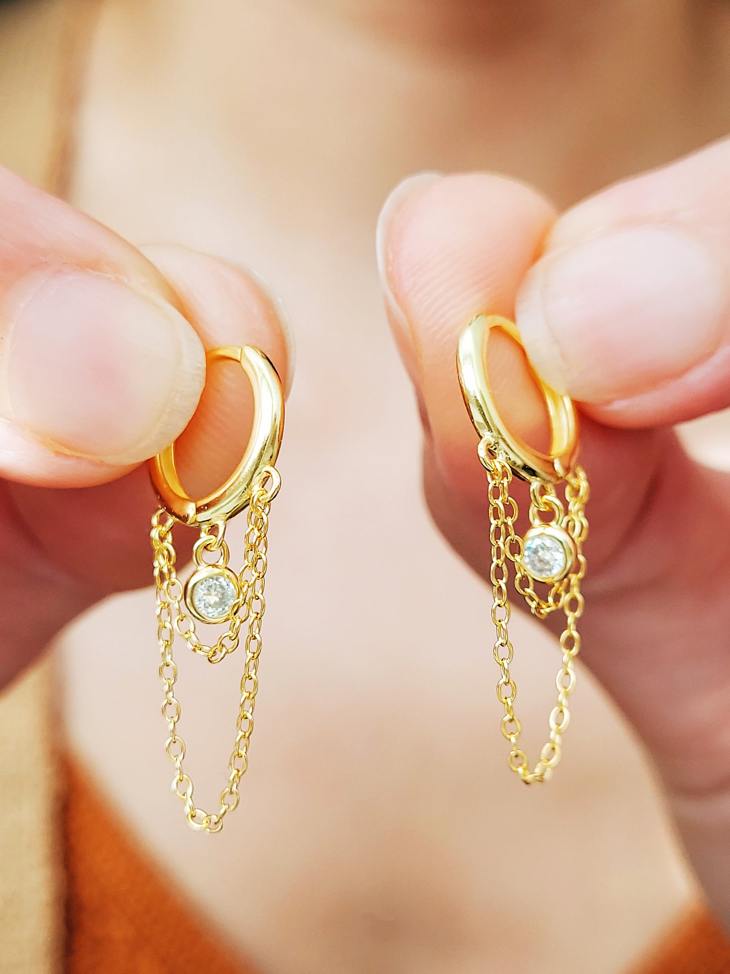 Close-up of a pair of gold double chain huggie earrings with a CZ diamond drop. Crafted in gold plated sterling silver, boho chic summer look.
