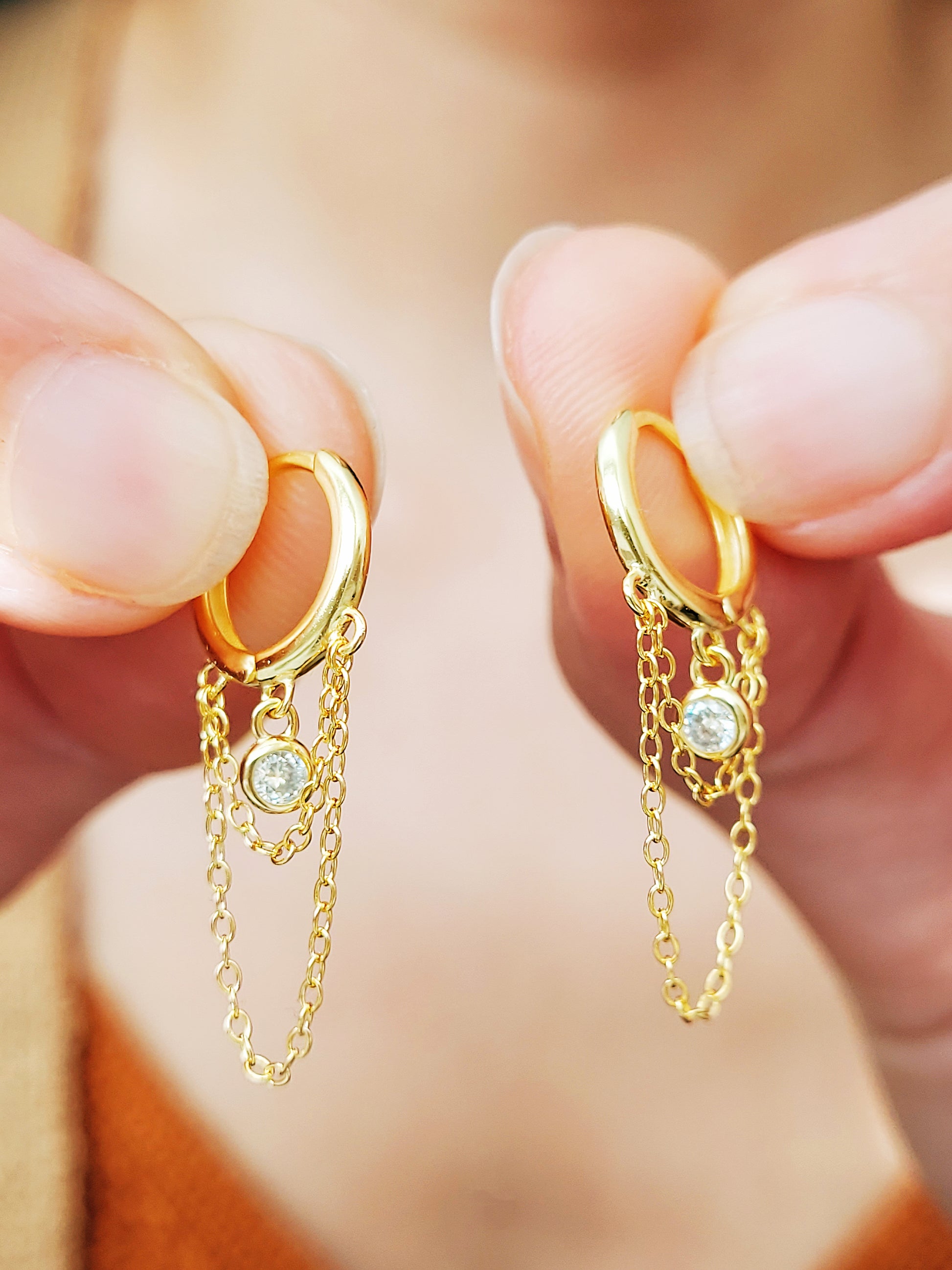 Close-up of a pair of gold double chain huggie earrings with a CZ diamond drop. Crafted in gold plated sterling silver, boho chic summer look.
