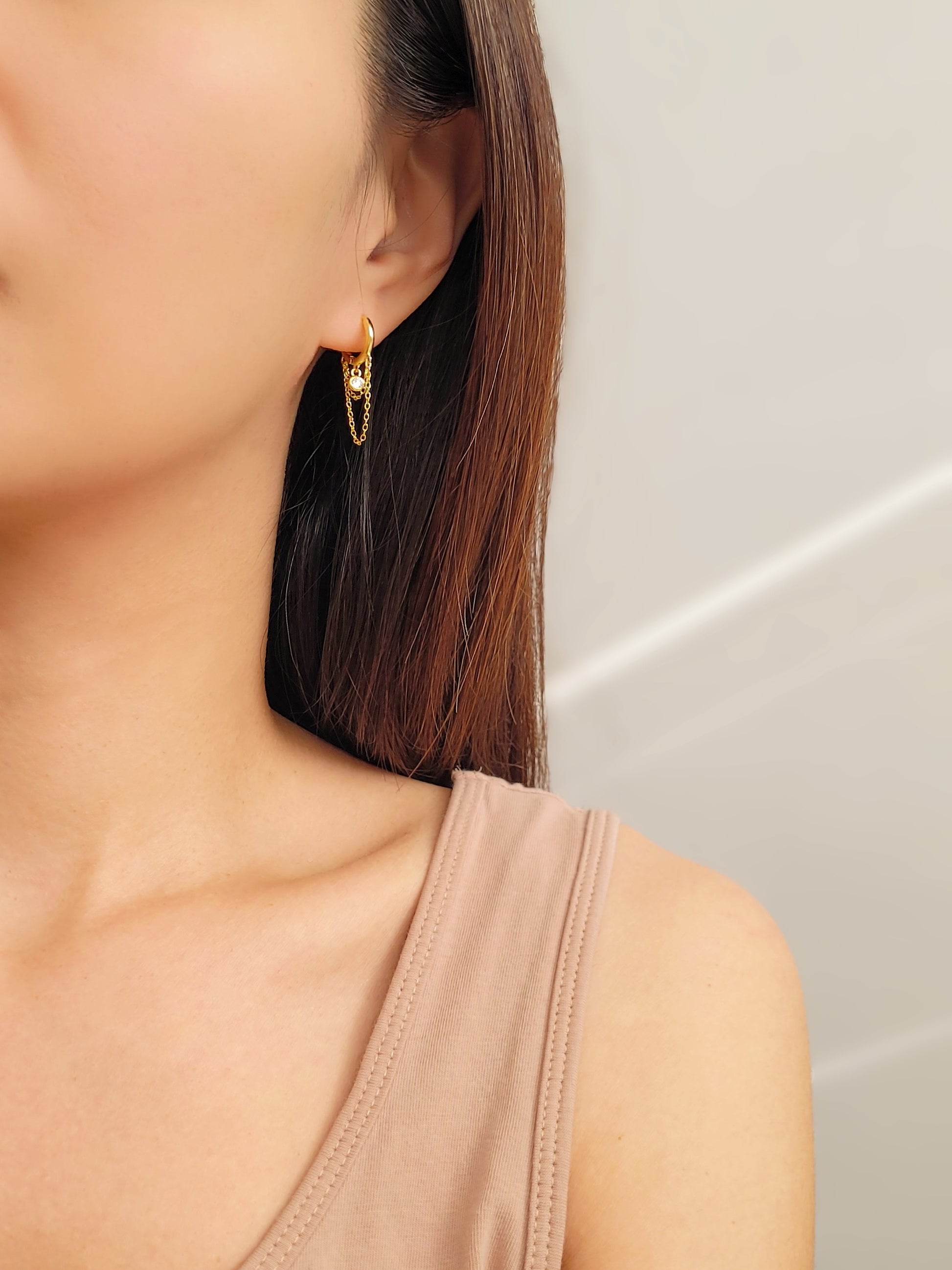 Close-up of a pair of gold double chain huggie earrings with a CZ diamond drop. Crafted in gold plated sterling silver, boho chic summer look.