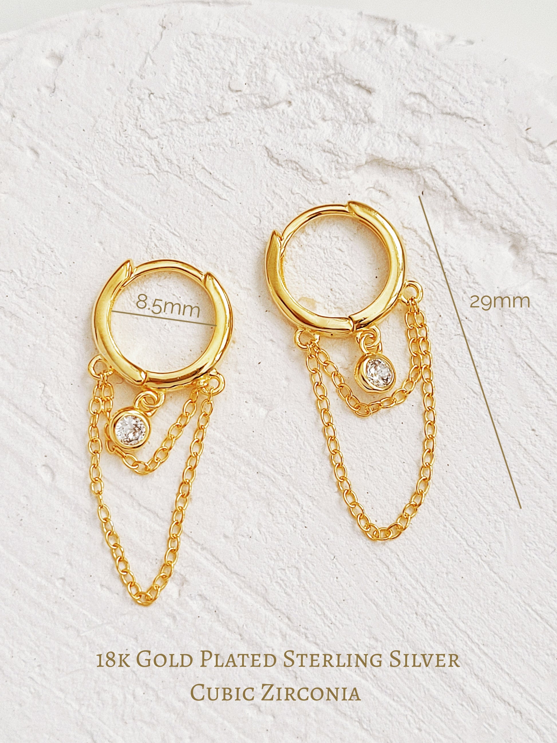 Close-up of a pair of gold double chain huggie earrings with a CZ diamond drop. Crafted in gold plated sterling silver, boho chic summer look.