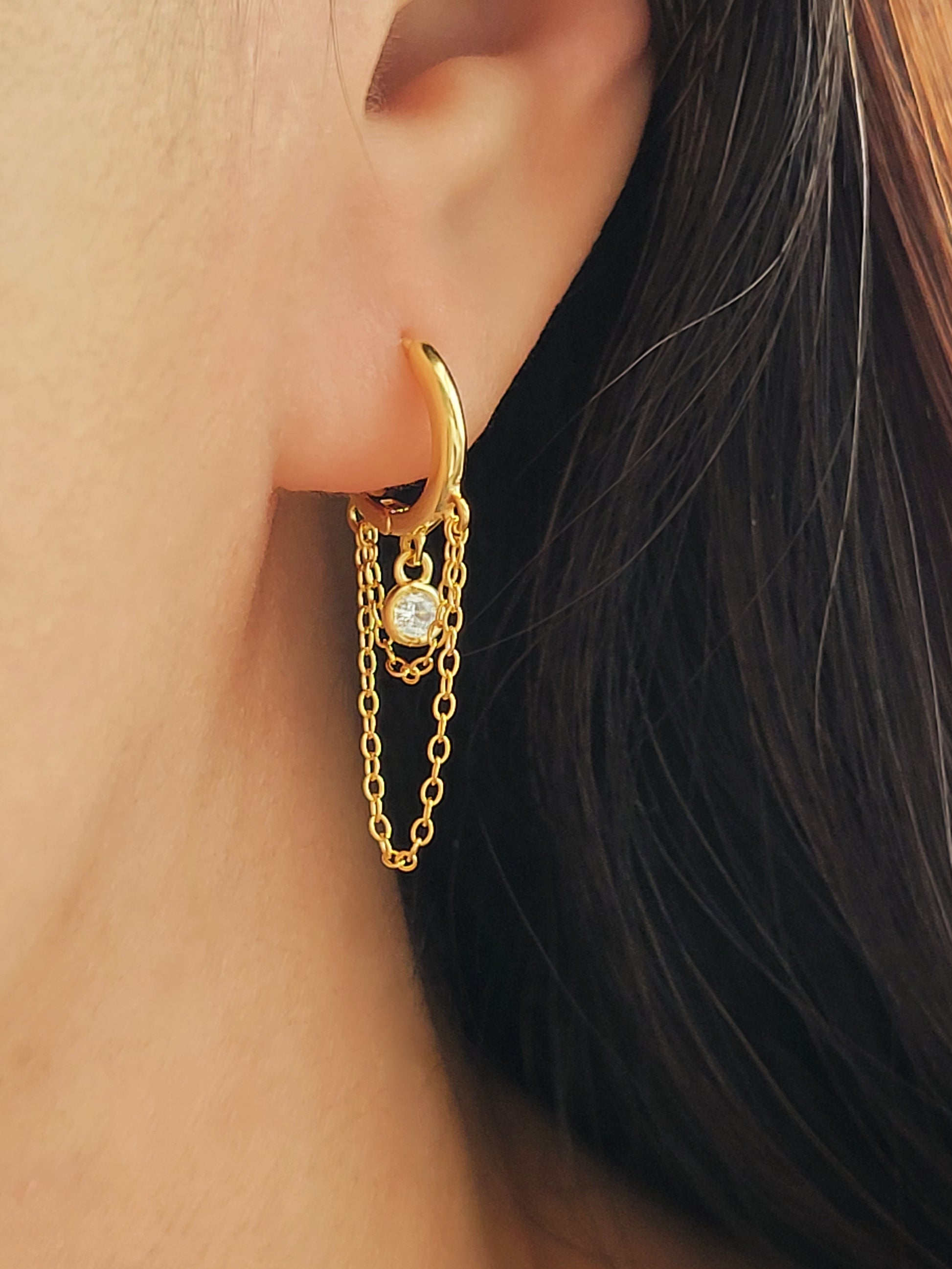 Close-up of a pair of gold double chain huggie earrings with a CZ diamond drop. Crafted in gold plated sterling silver, boho chic summer look.