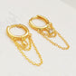 Close-up of a pair of gold double chain huggie earrings with a CZ diamond drop. Crafted in gold plated sterling silver, boho chic summer look.