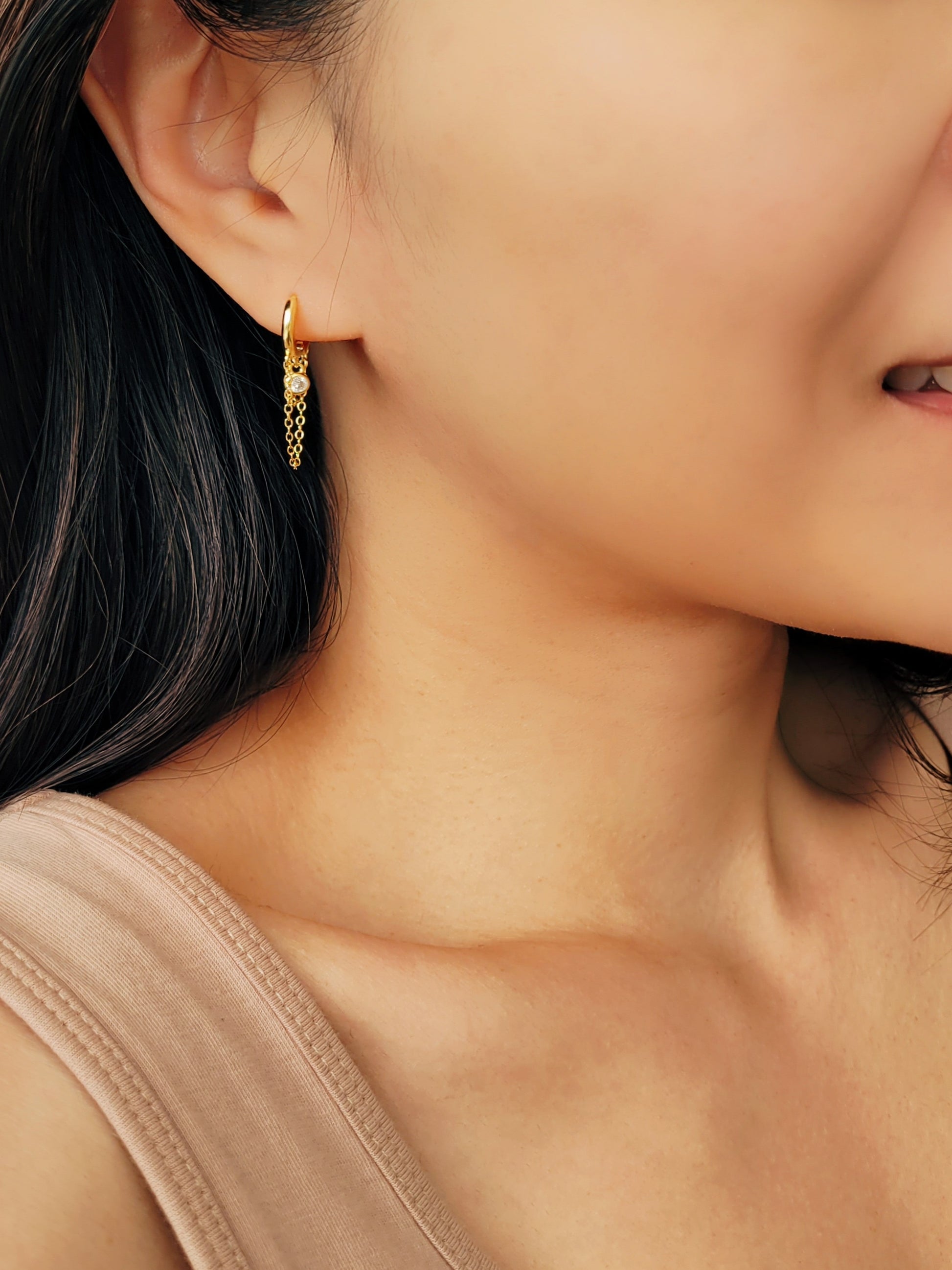 Close-up of a pair of gold double chain huggie earrings with a CZ diamond drop. Crafted in gold plated sterling silver, boho chic summer look.