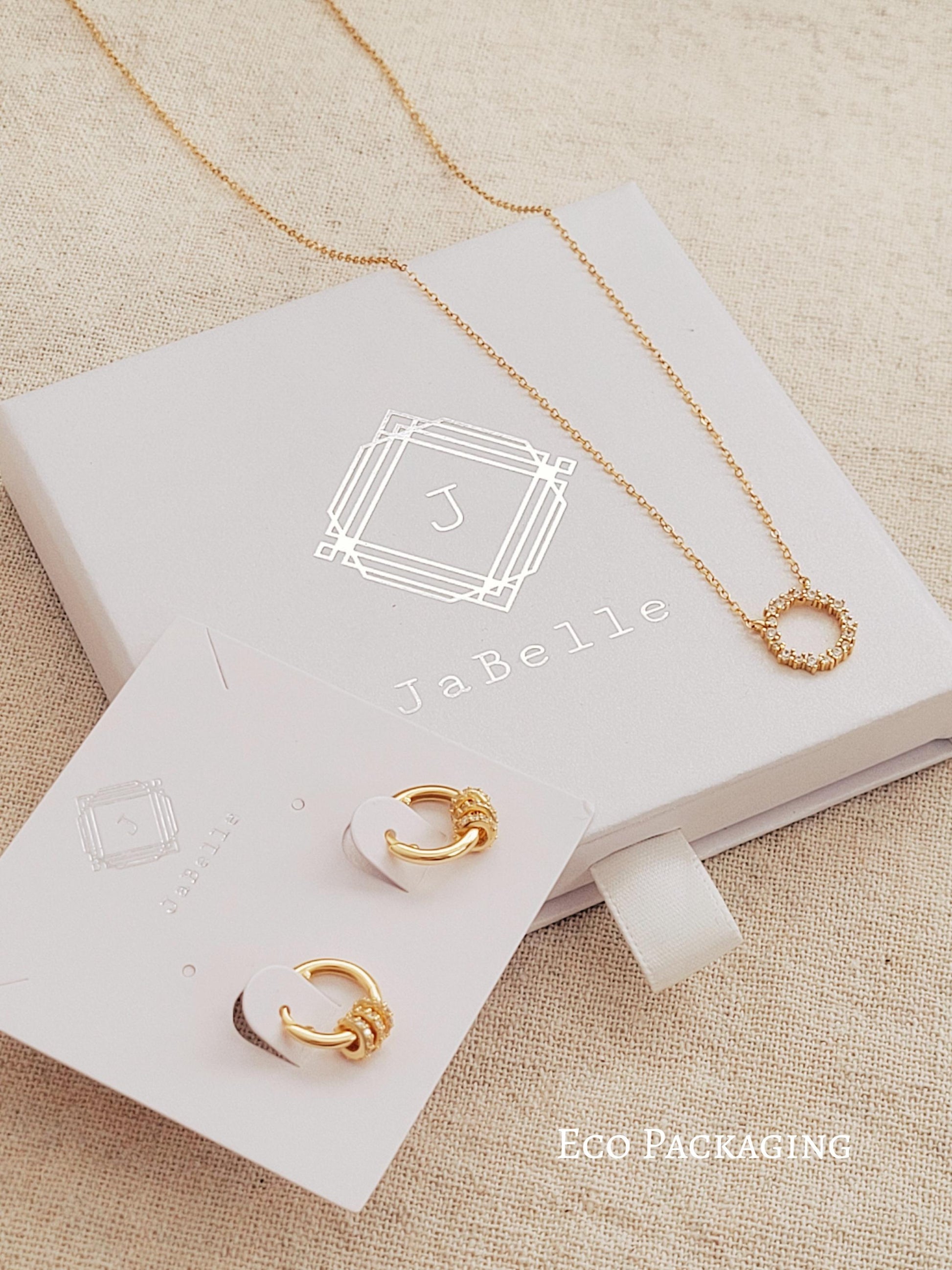 Gold necklace and earrings on a JaBelle branded jewelry box with eco-friendly packaging label.