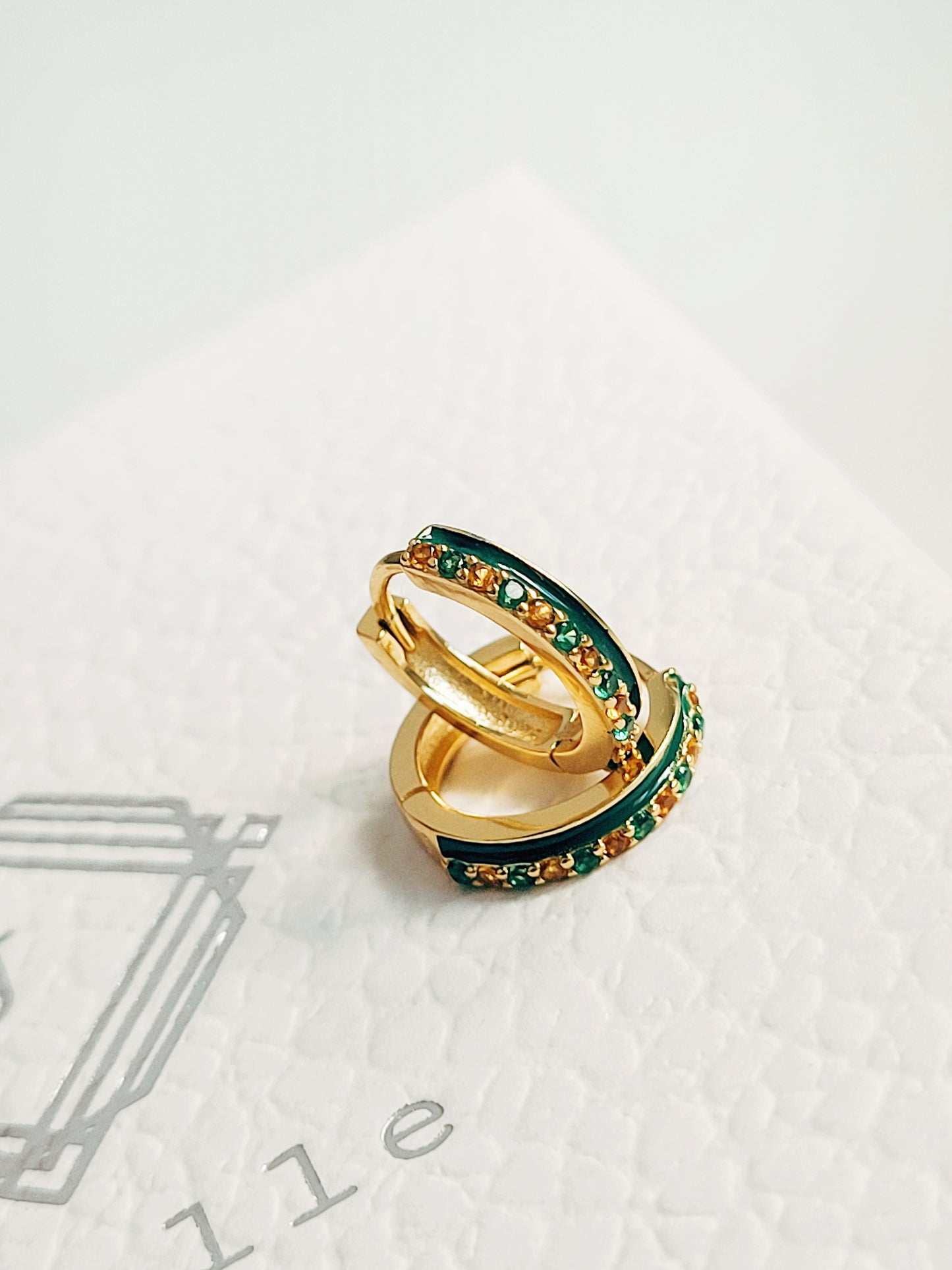 Close-up of emerald green enamel huggie hoop earrings with gold-plated and zircons detailing, showcasing its elegance minimalist style.