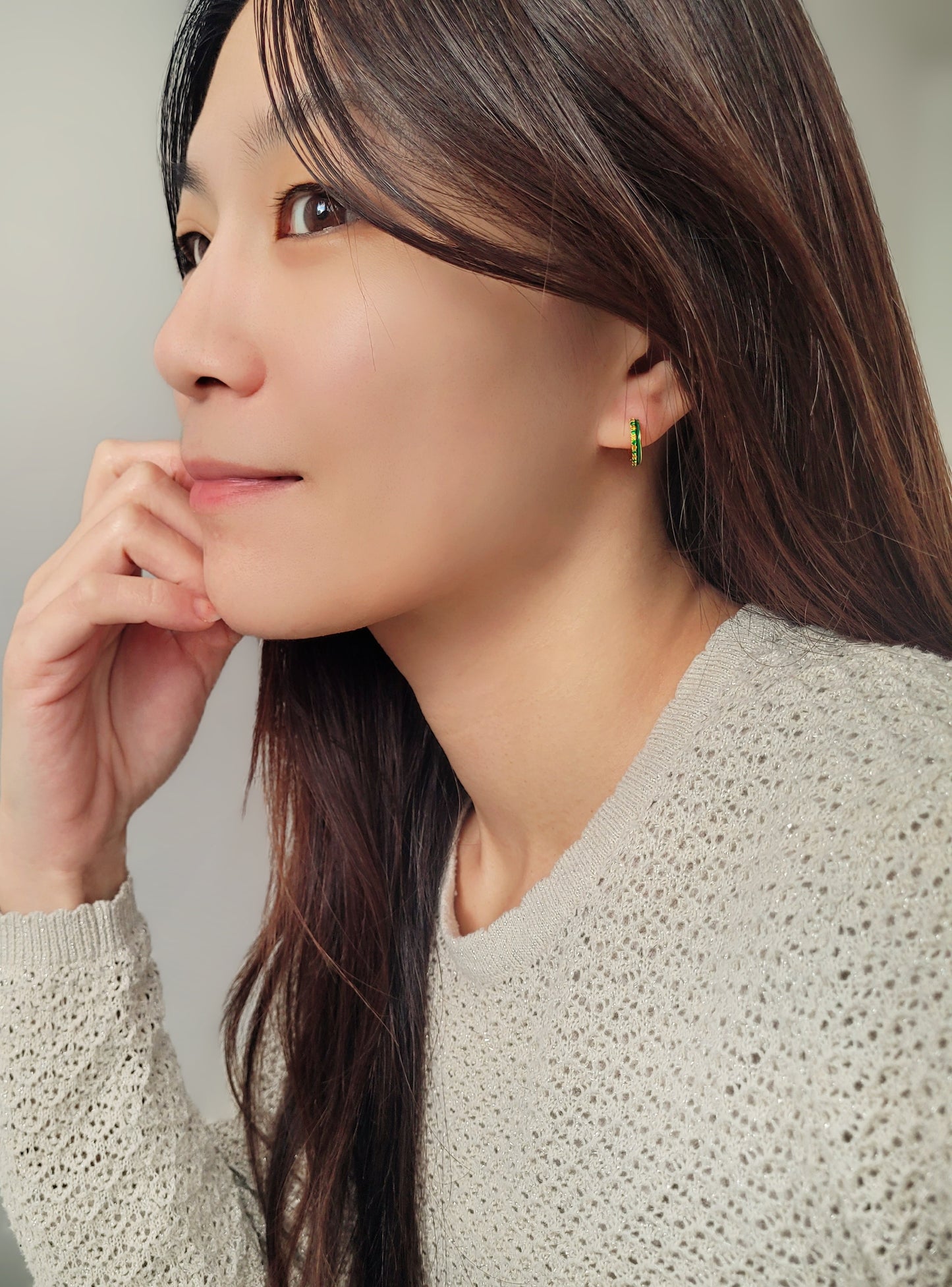 A woman wearing vintage inspired emerald green enamel hoops styled with a cozy sweater.