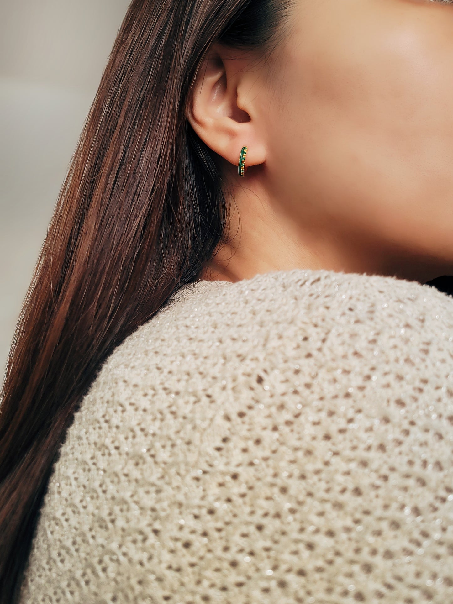 Elegant small gold huggie hoops featuring a vibrant green enamel design with green and yellow crystals paved.